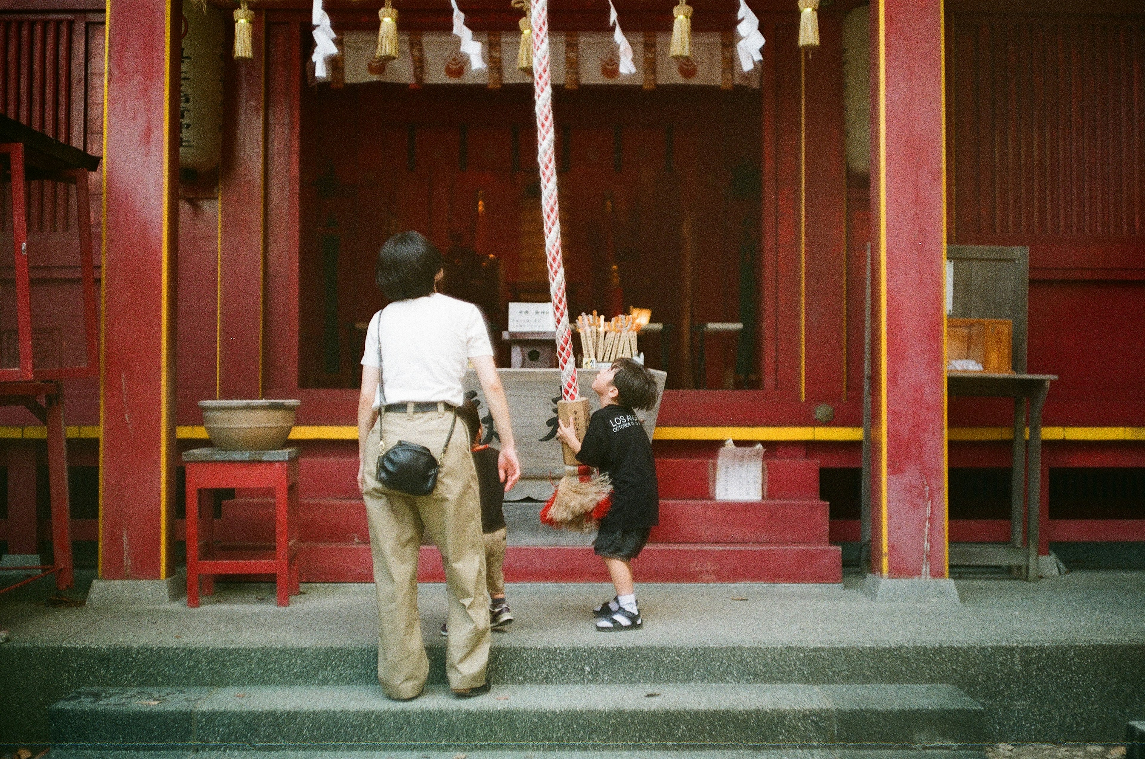 神社の前で遊ぶ子供と大人の後ろ姿 赤い壁と装飾が特徴的