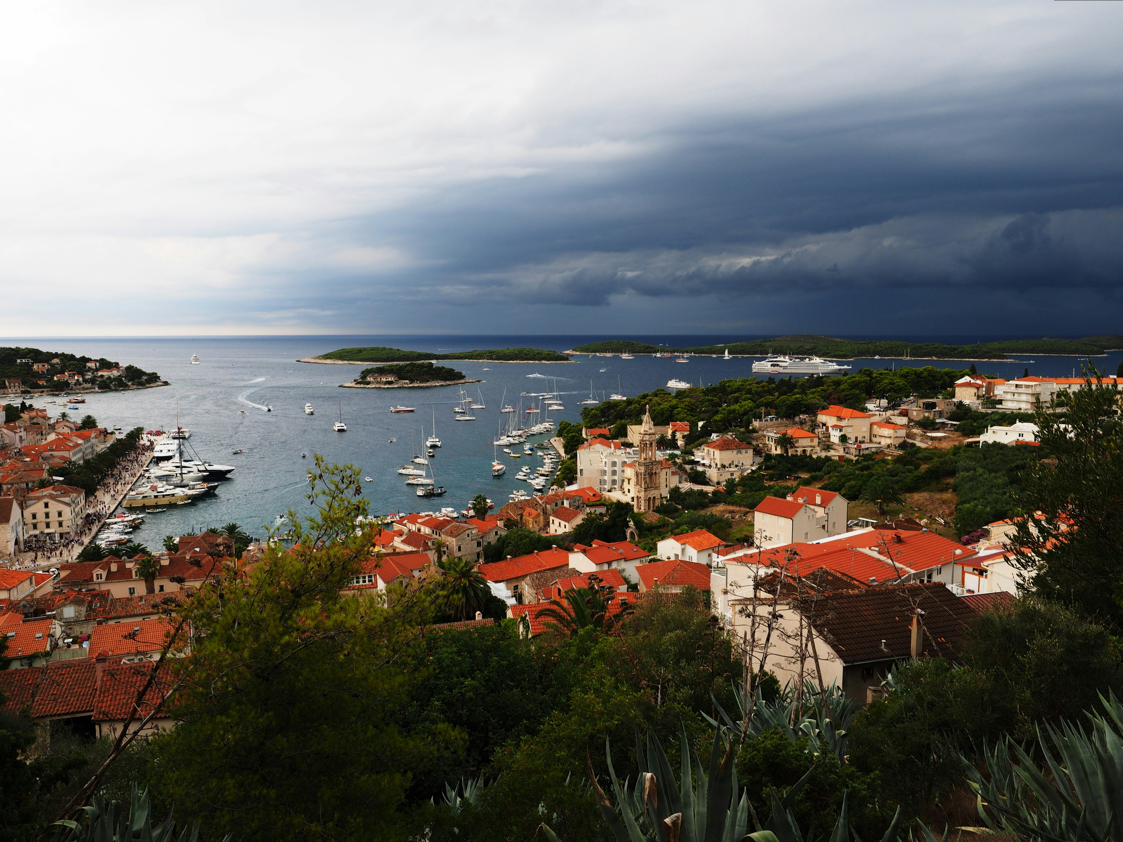 Scenic view of a coastal town with red rooftops and dark stormy skies