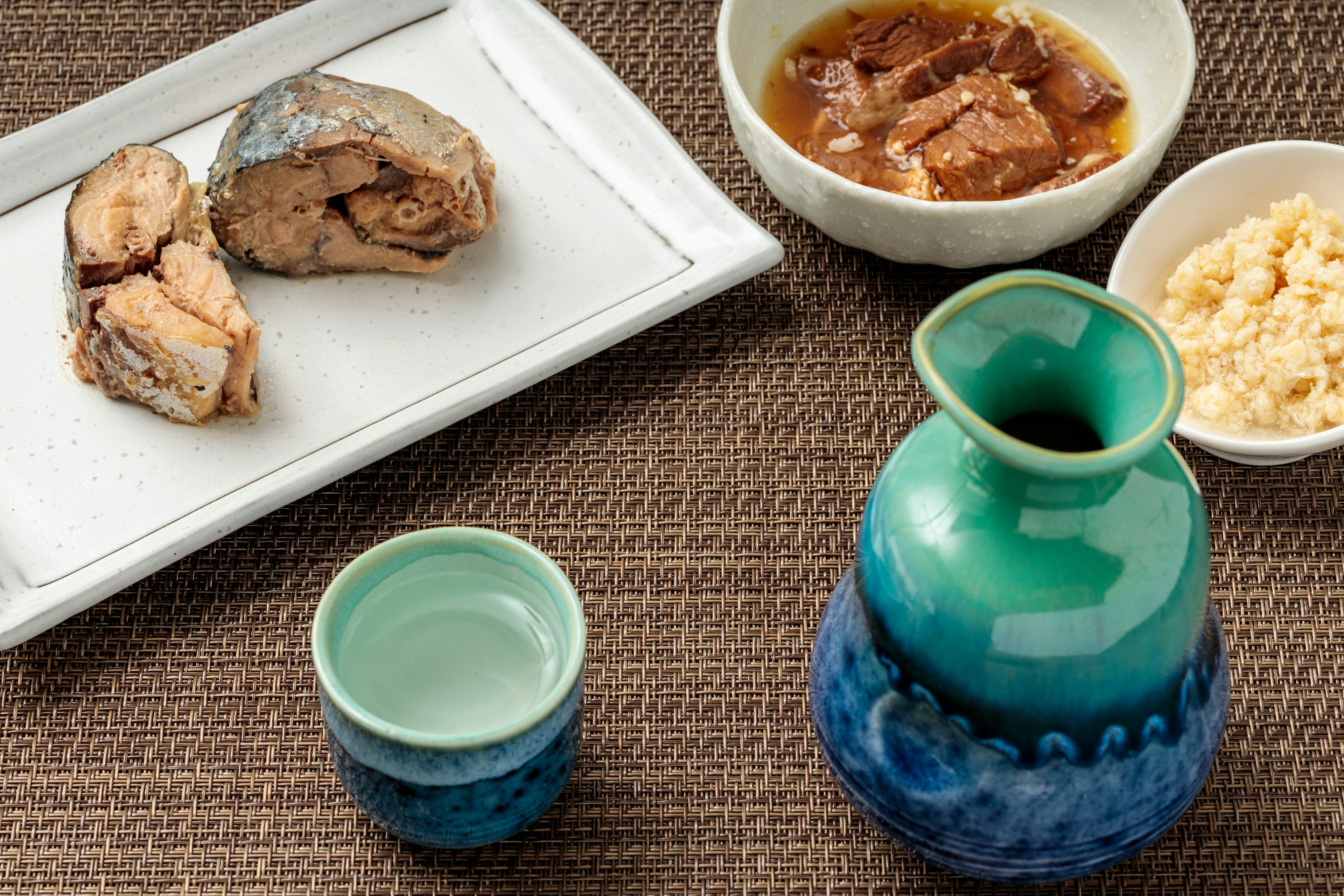 Botella de sake de cerámica azul y taza junto a platos de pescado y carne