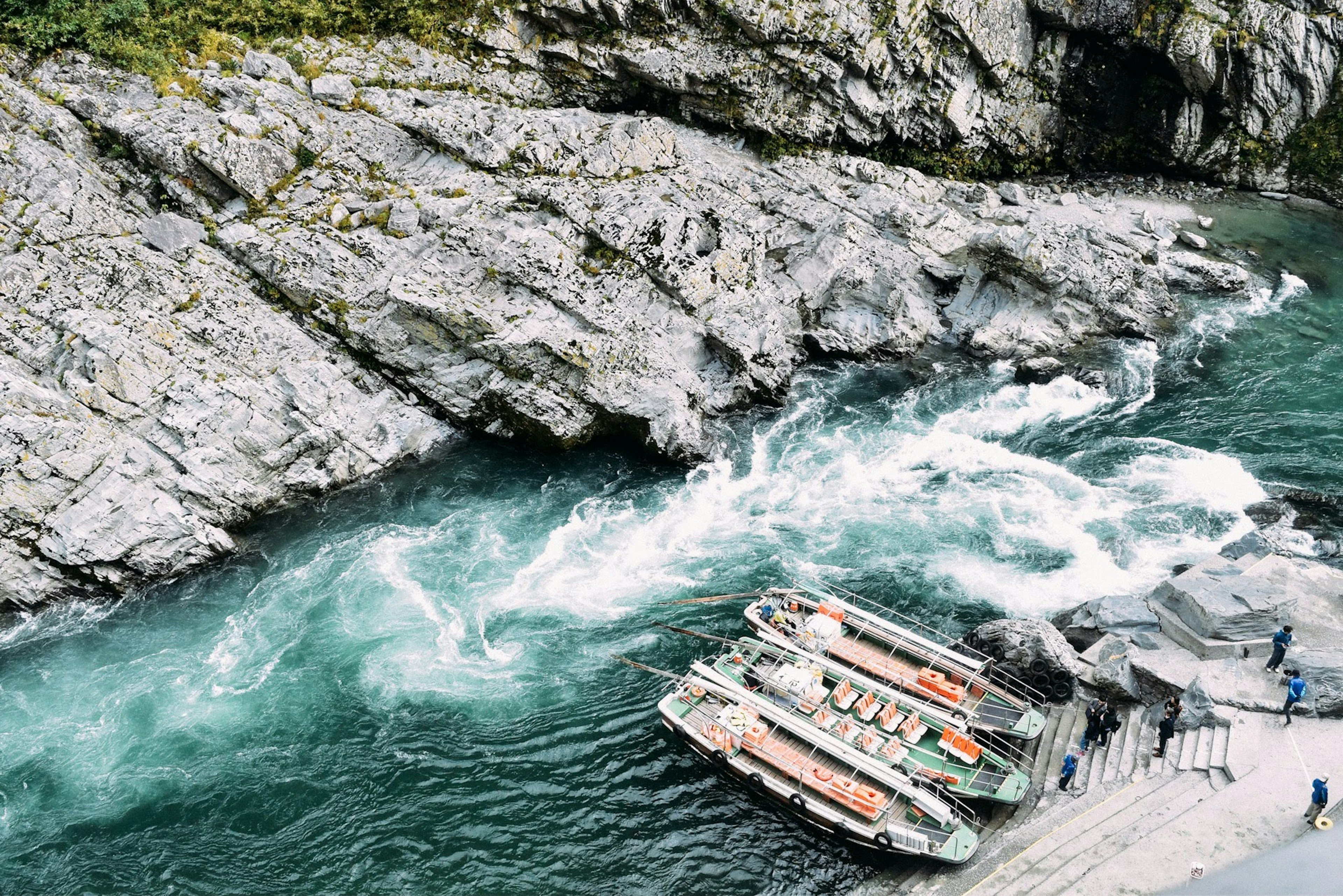 Scene of a river rapids and boats docked at rocky shore