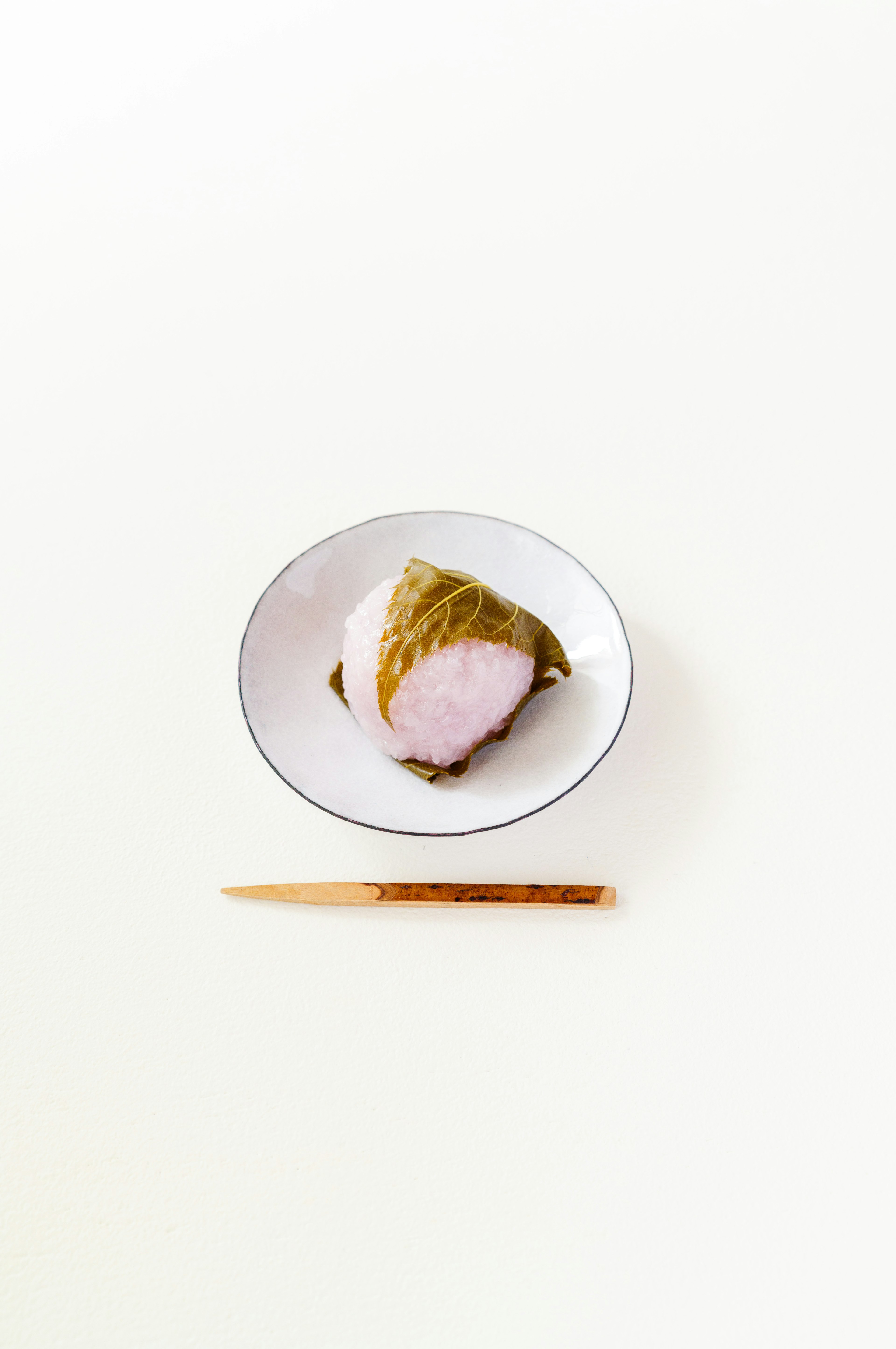 Piring sakura mochi dengan sumpit kayu di atas latar belakang putih