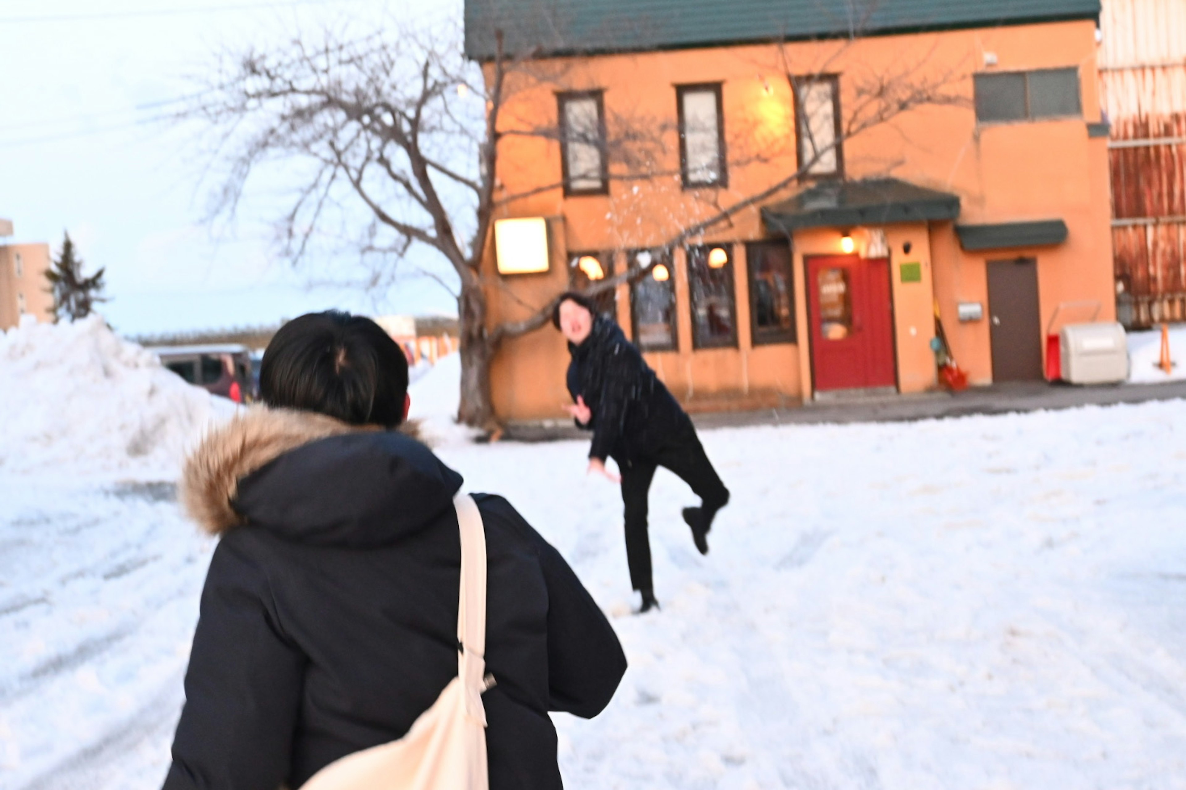 Zwei Personen spielen im Schnee mit einem Gebäude im Hintergrund