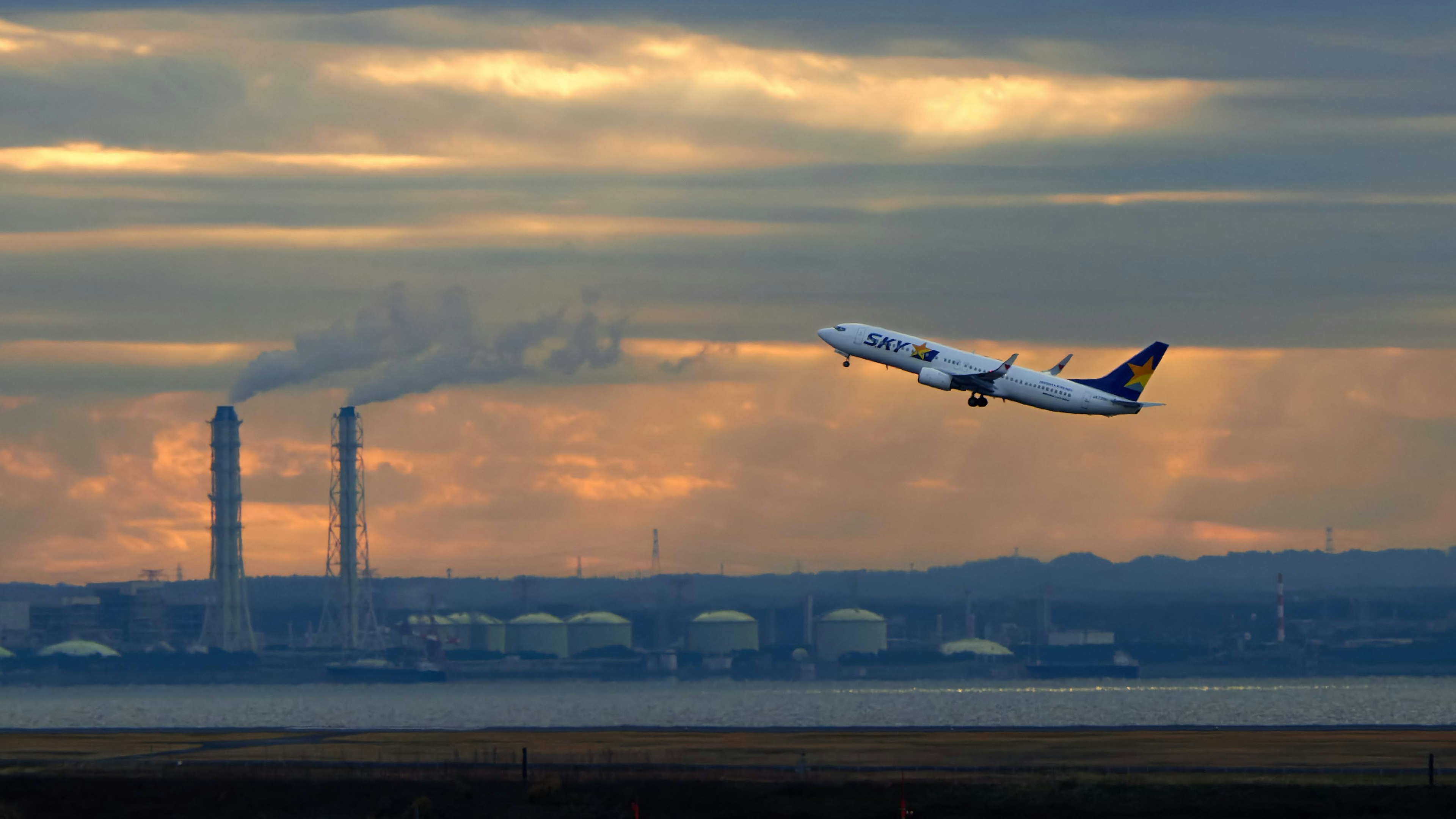 Avión despegando contra un cielo de atardecer con chimeneas al fondo