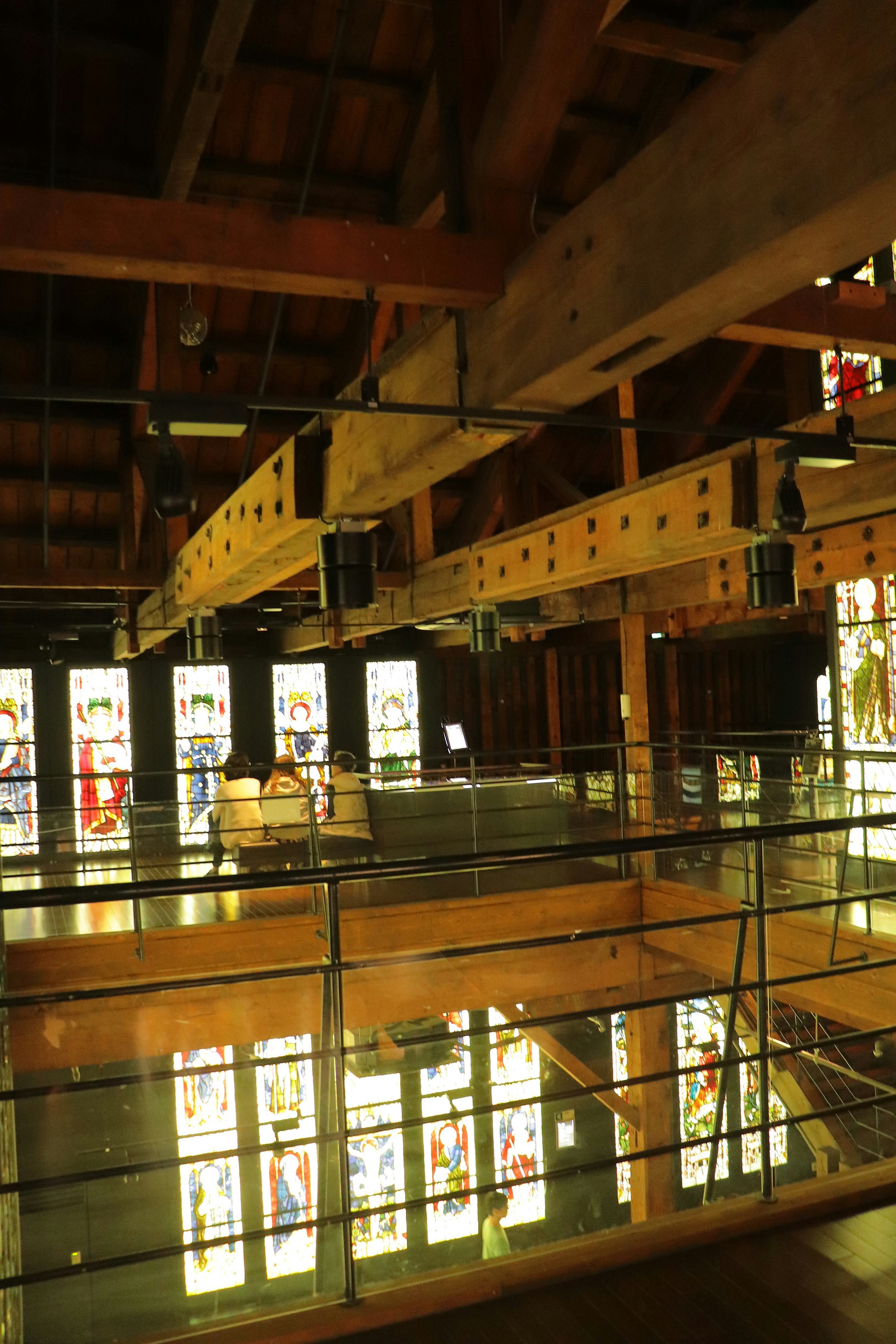 Interior de un edificio de madera con grandes ventanas de vitrales y barandilla de vidrio