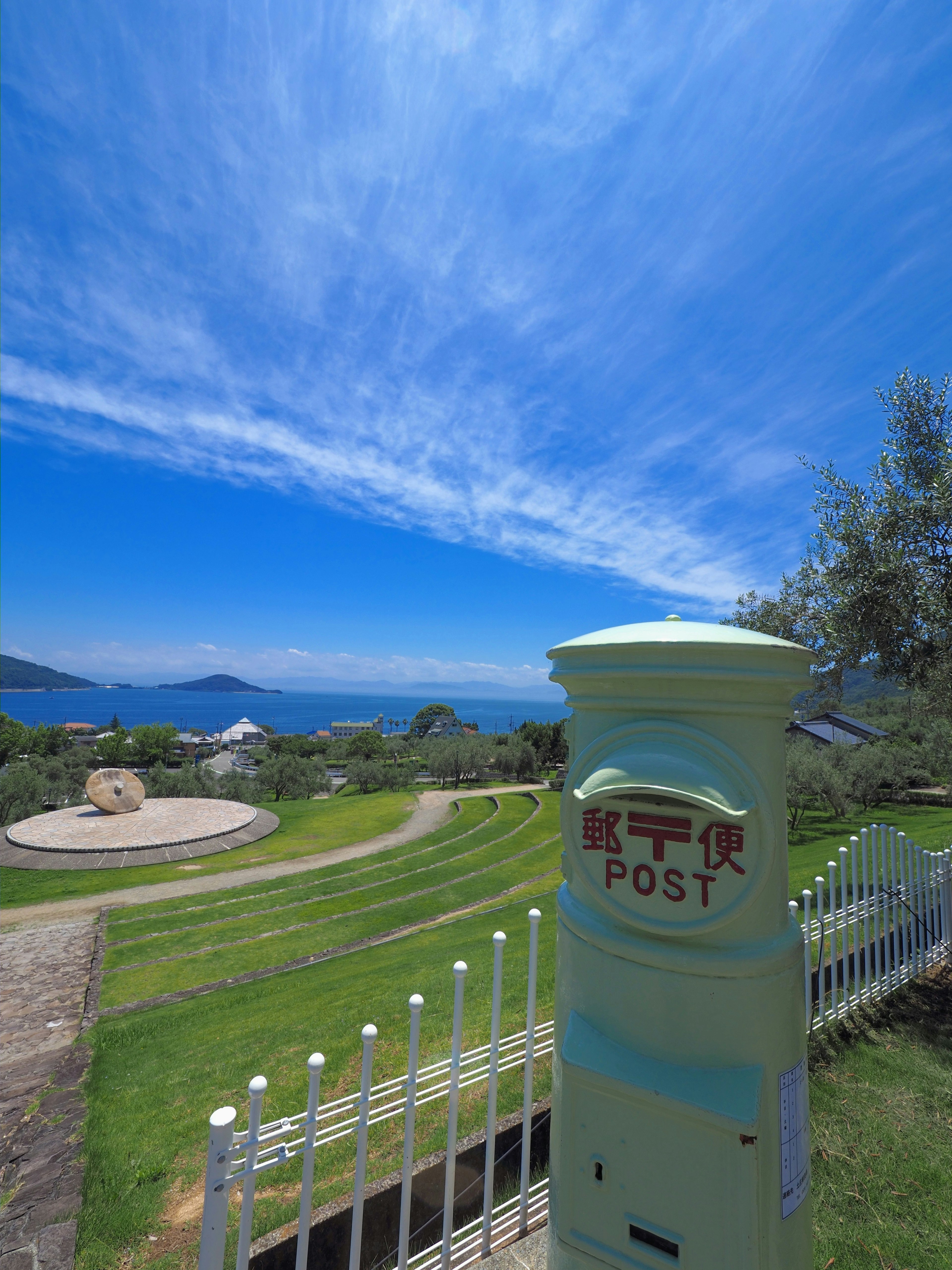 Cassetta postale verde con caratteri giapponesi sotto un cielo blu luminoso con nuvole