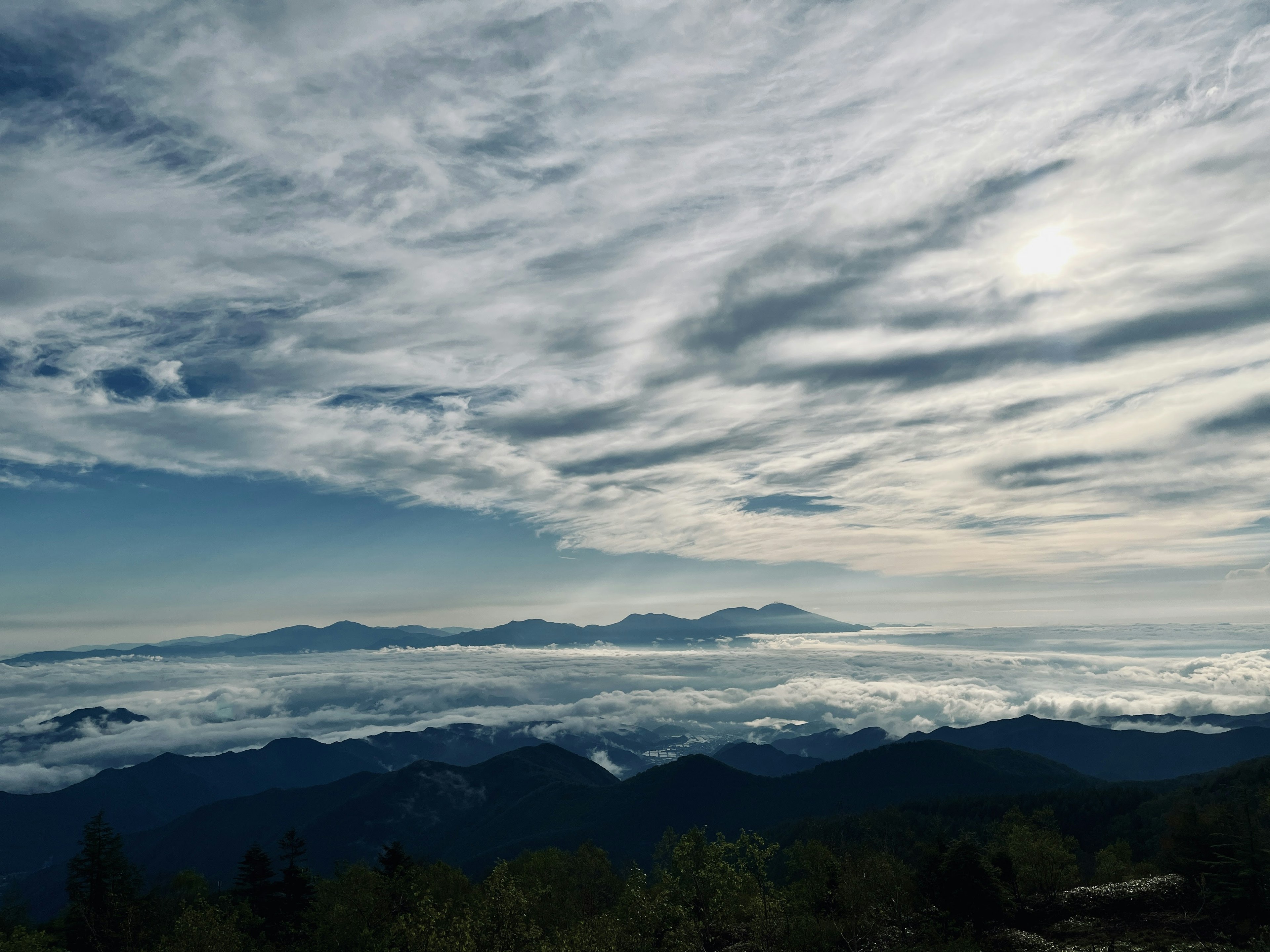 Pemandangan pegunungan di bawah lapisan awan dengan langit biru