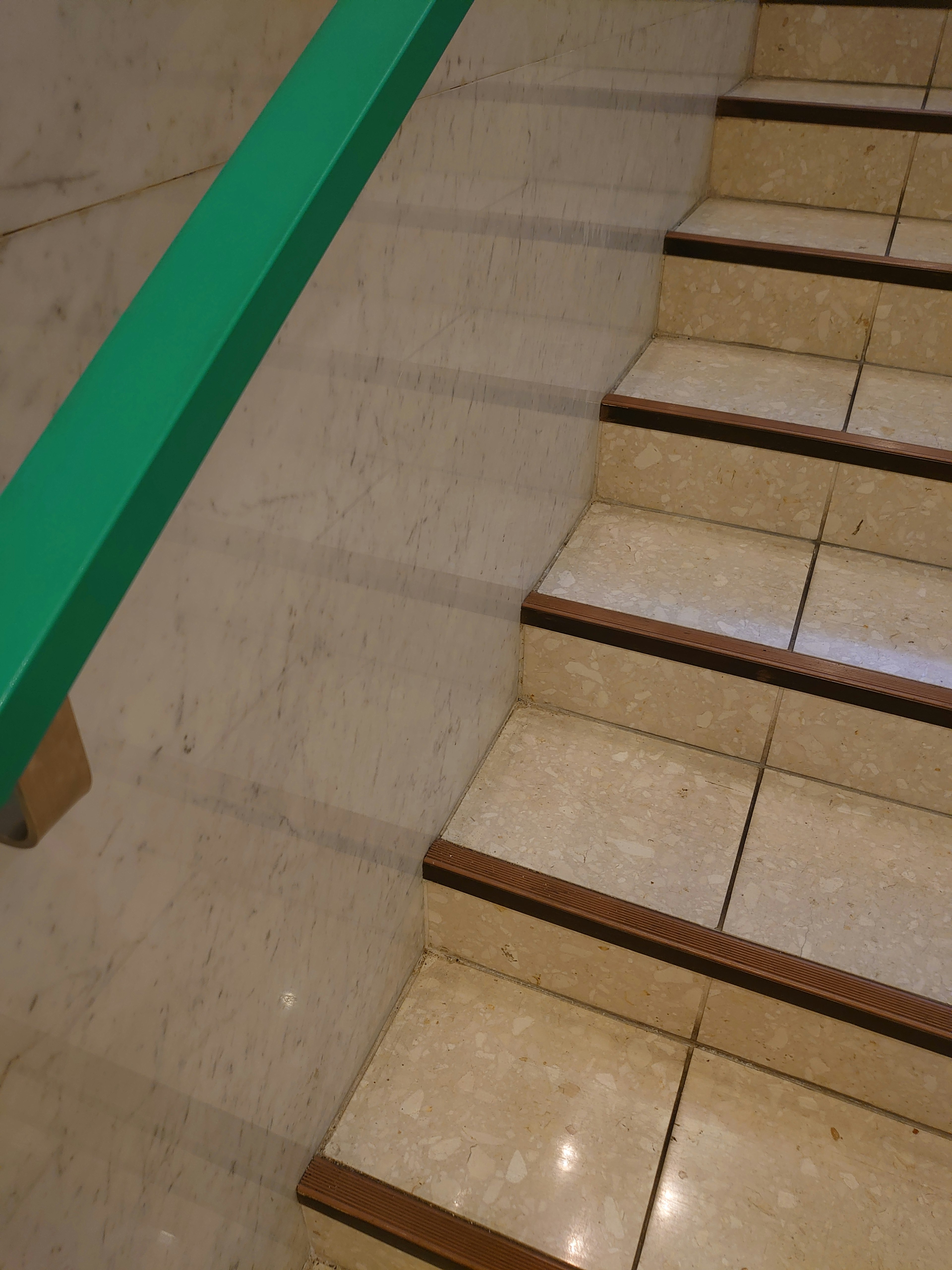 Image of stairs with glossy tiles and a green handrail