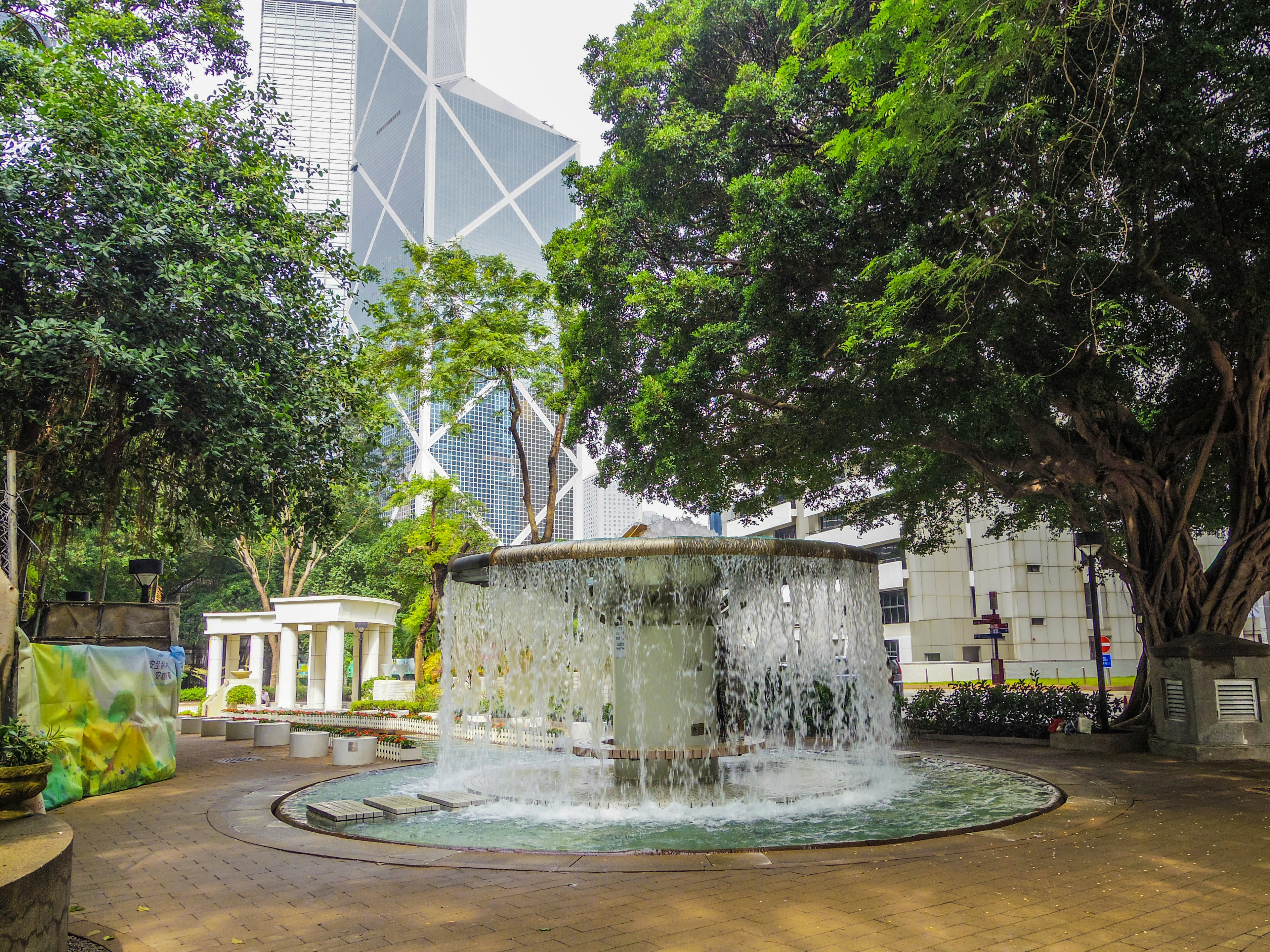 A fountain surrounded by lush trees with a skyscraper in the background