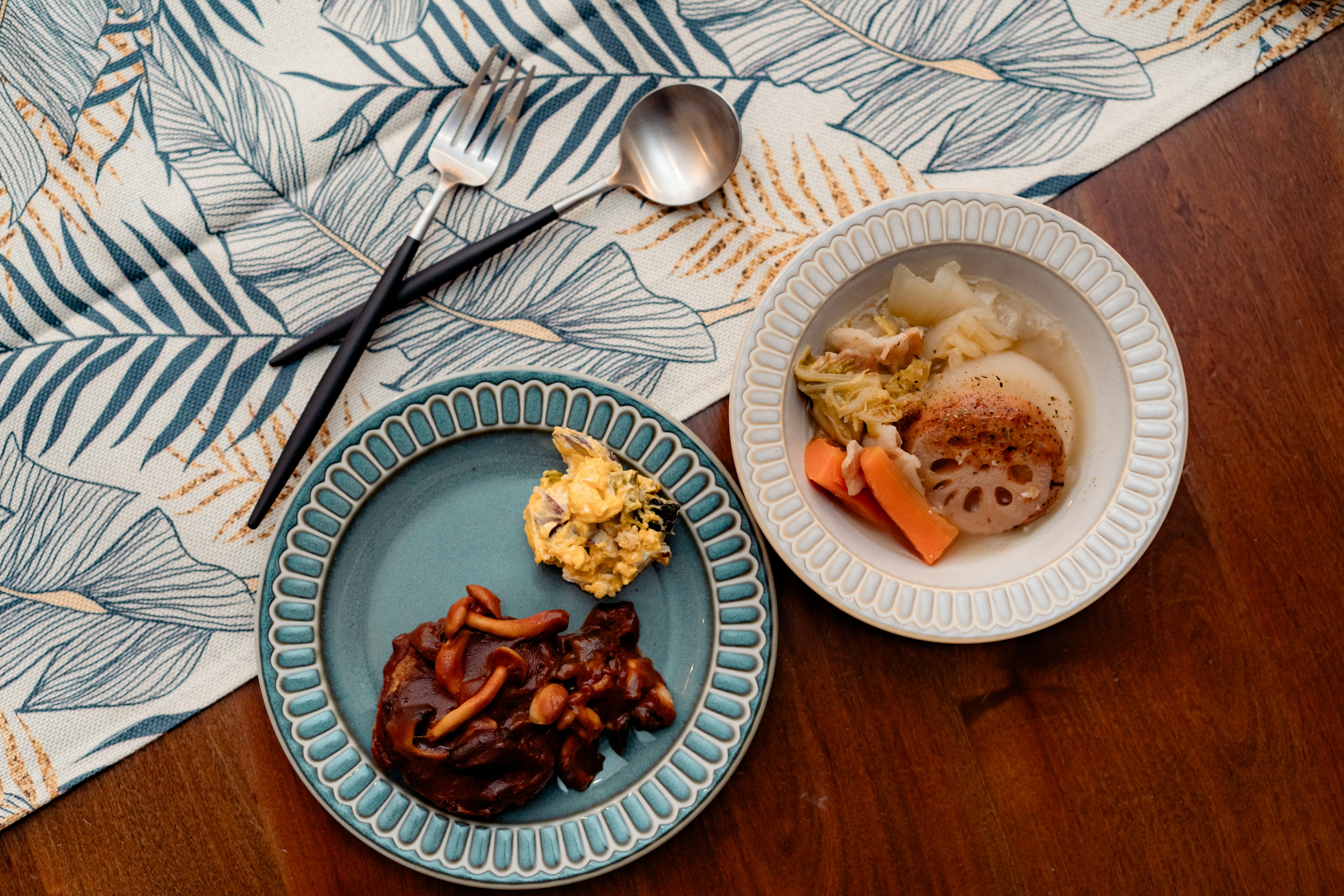 Blue plate with meat dish and egg dish White plate with vegetable and lotus root dish Leaf-patterned tablecloth