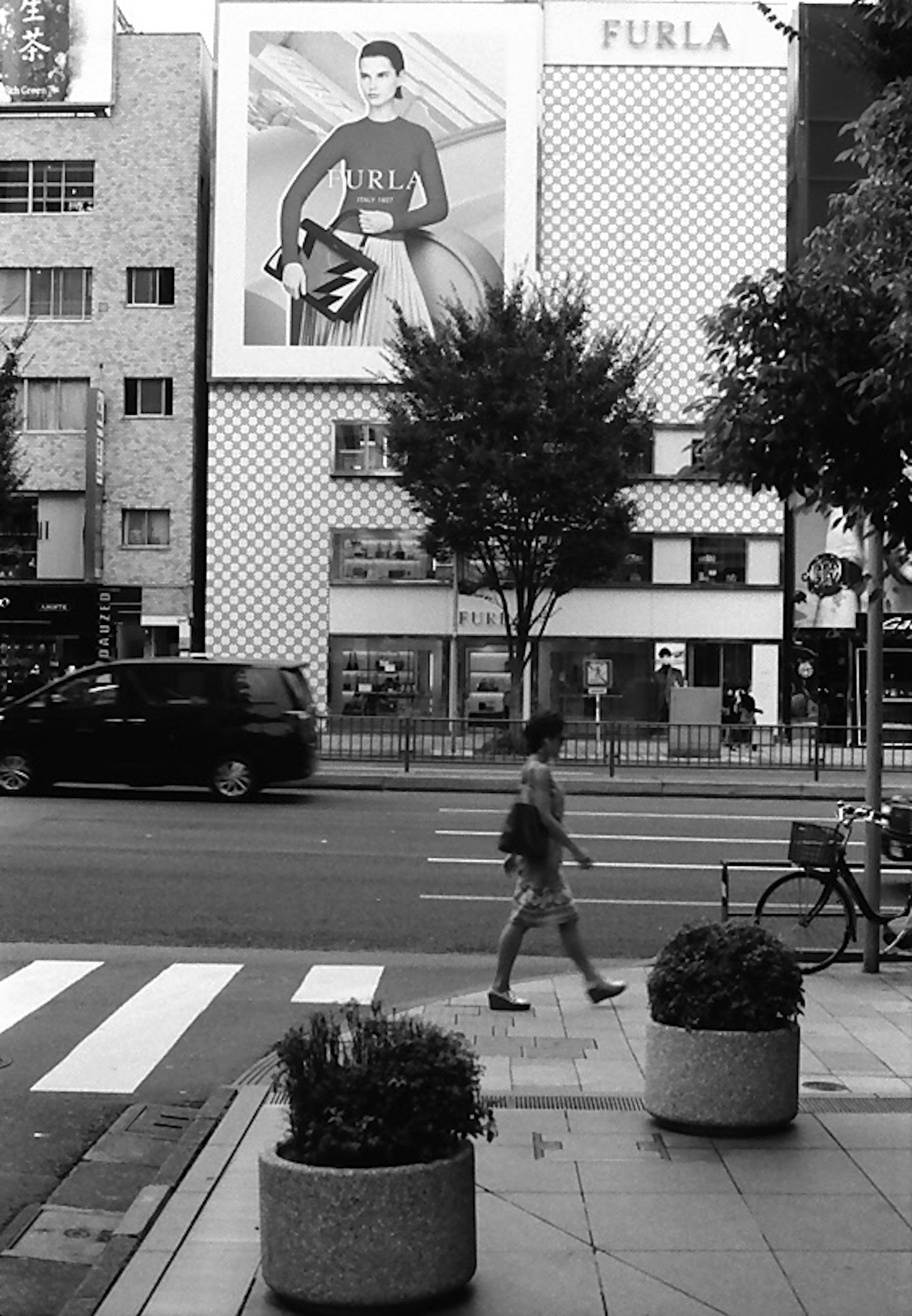 A person walking across a crosswalk with a FURLA billboard in the background