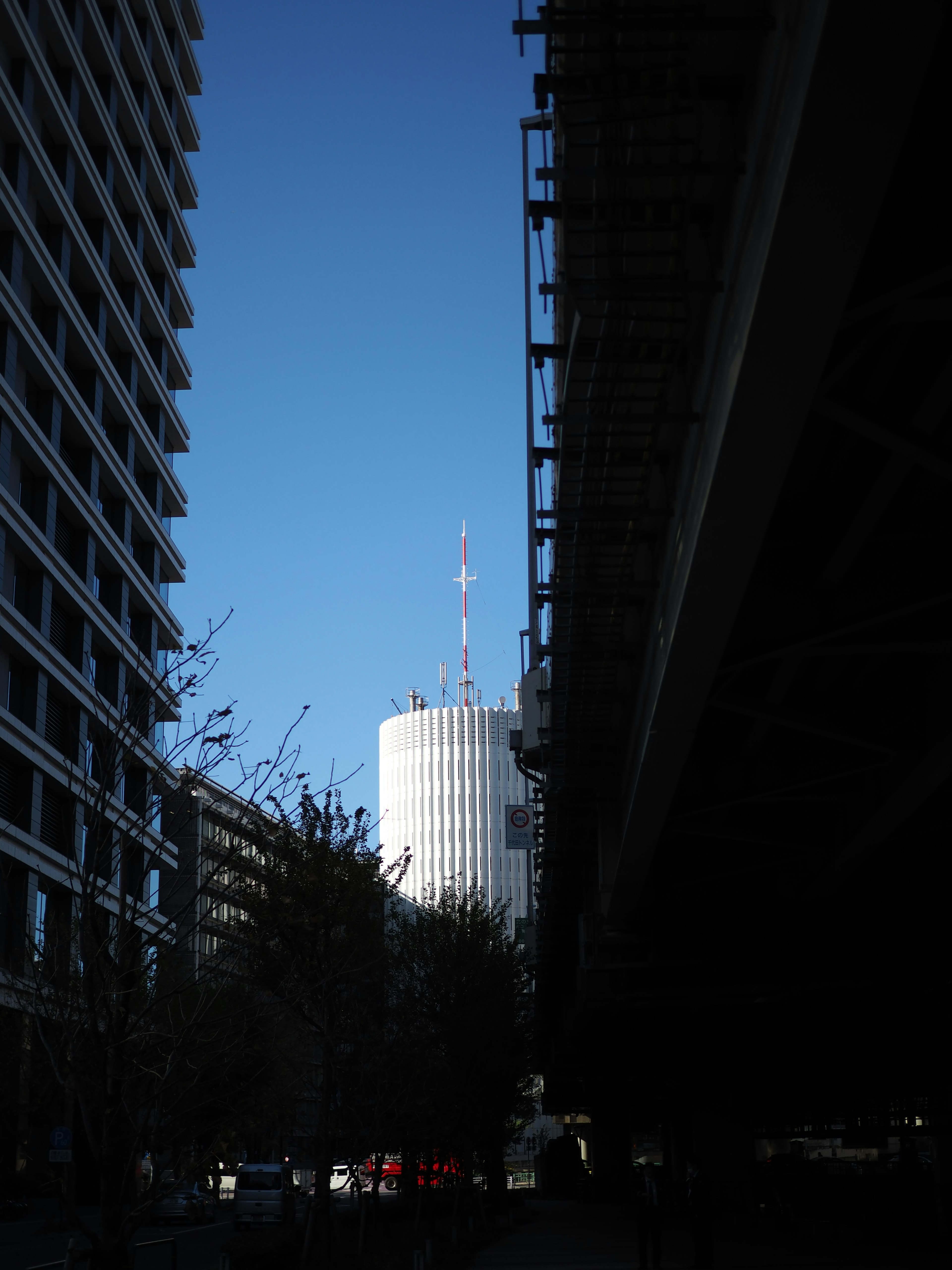 明るい青空の下に立つ高層ビルのシルエットと周囲の建物