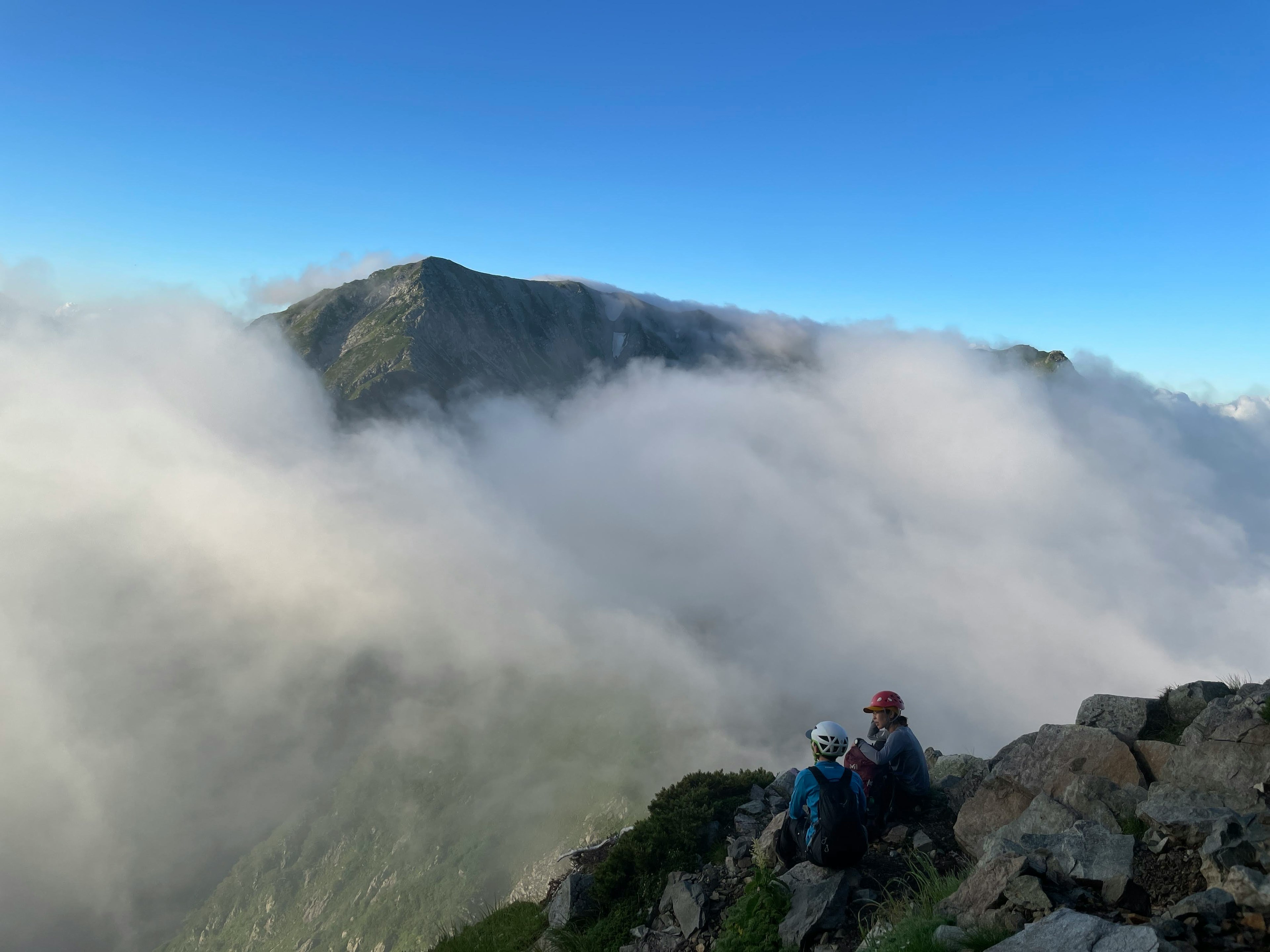 Dos excursionistas sentados en la cima de una montaña rodeados de nubes