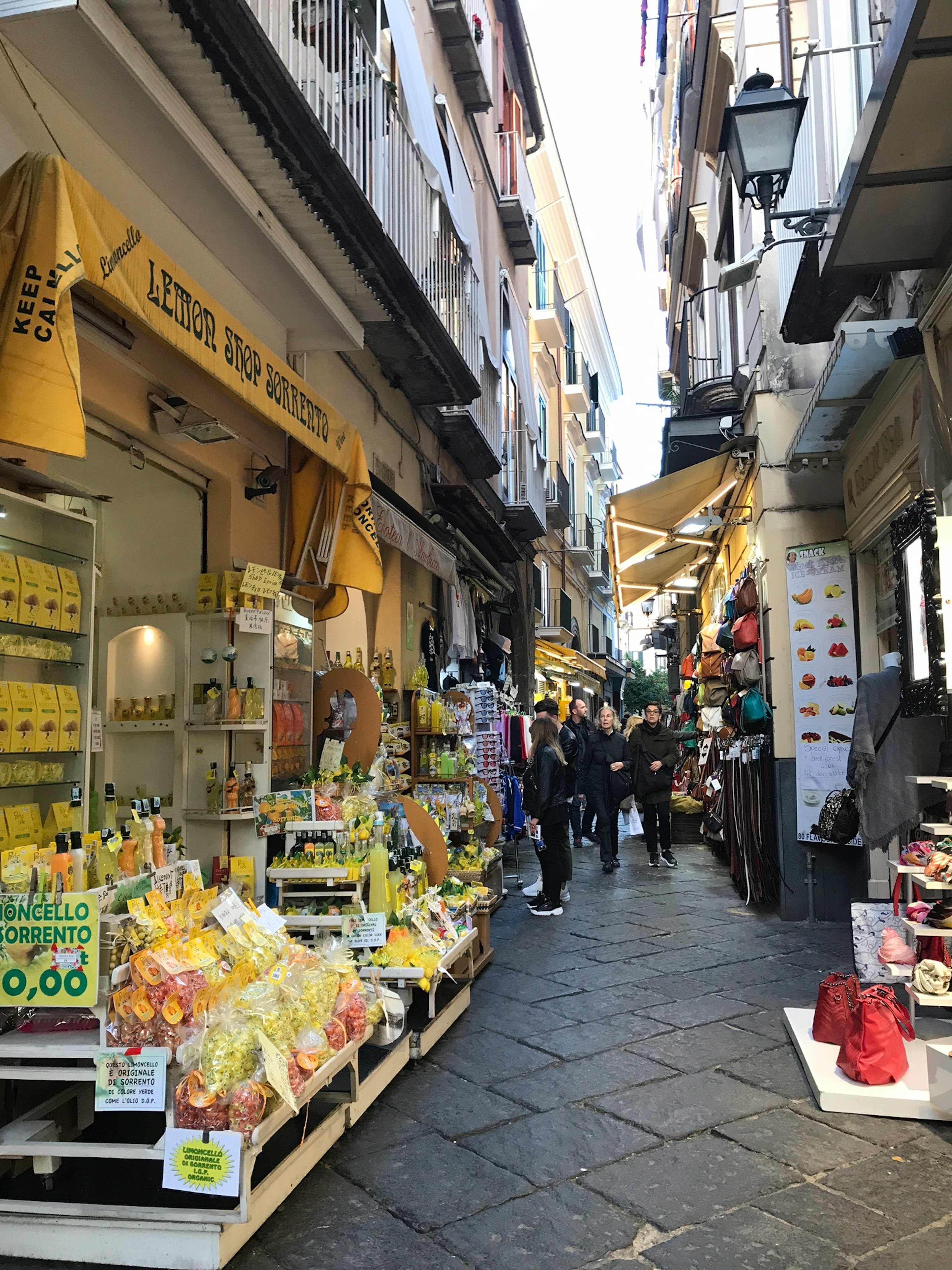 Strada stretta fiancheggiata da negozi di frutta e limoni con gente affollata