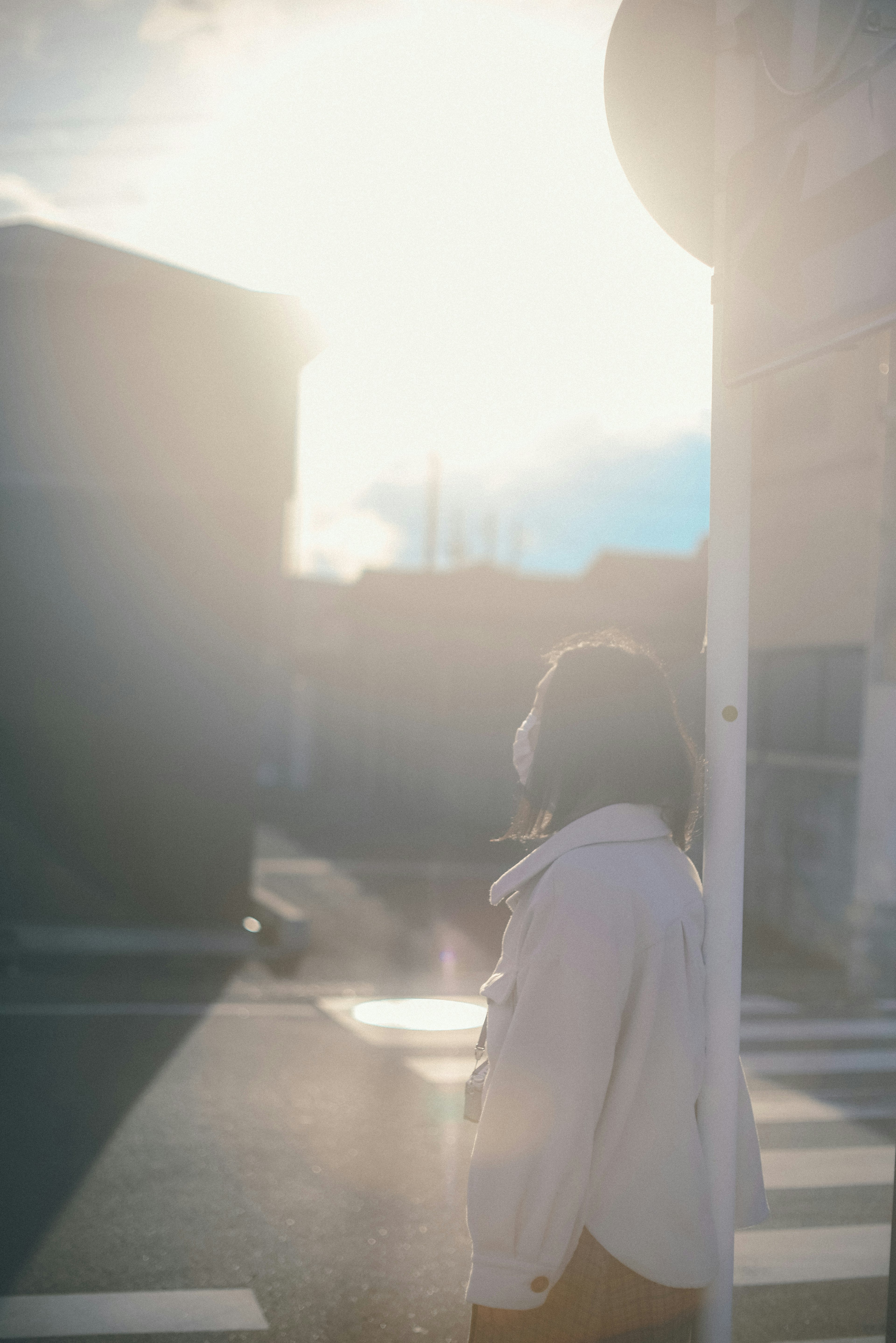 A woman standing at a street corner basking in sunlight