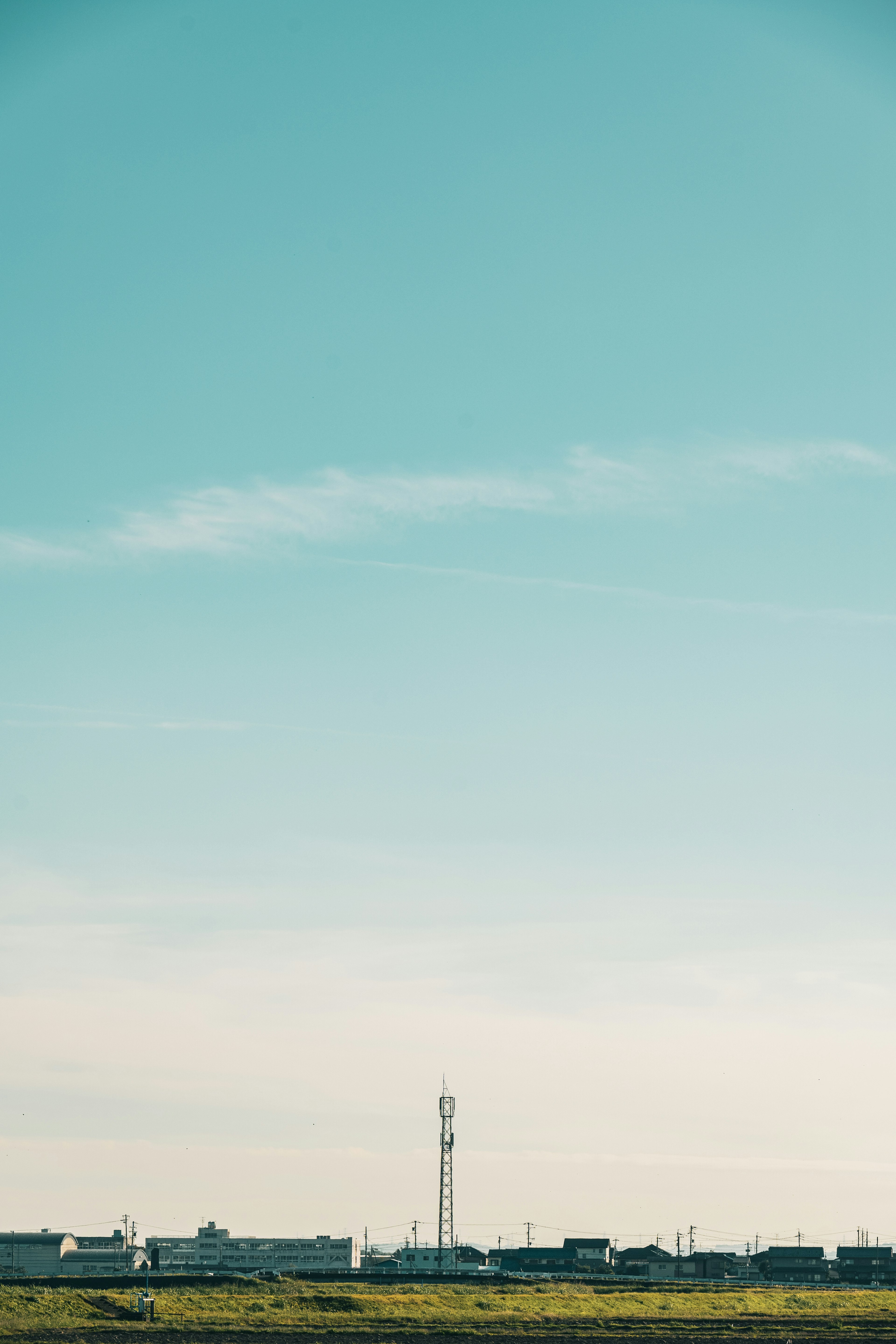 Landschaft mit blauem Himmel und grünem Feld mit einem Sendemast und Gebäuden