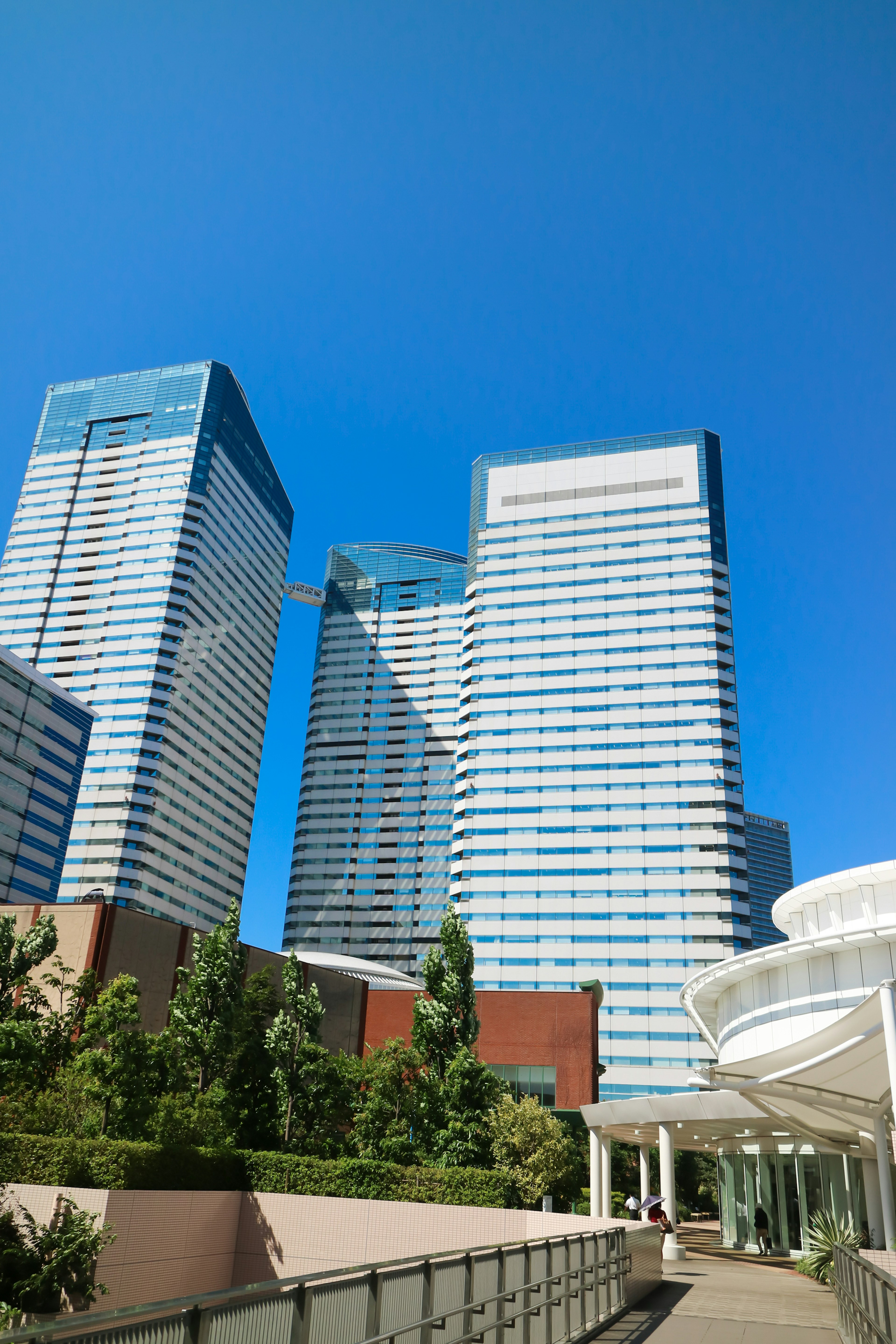 Cityscape featuring towering skyscrapers under a clear blue sky with greenery