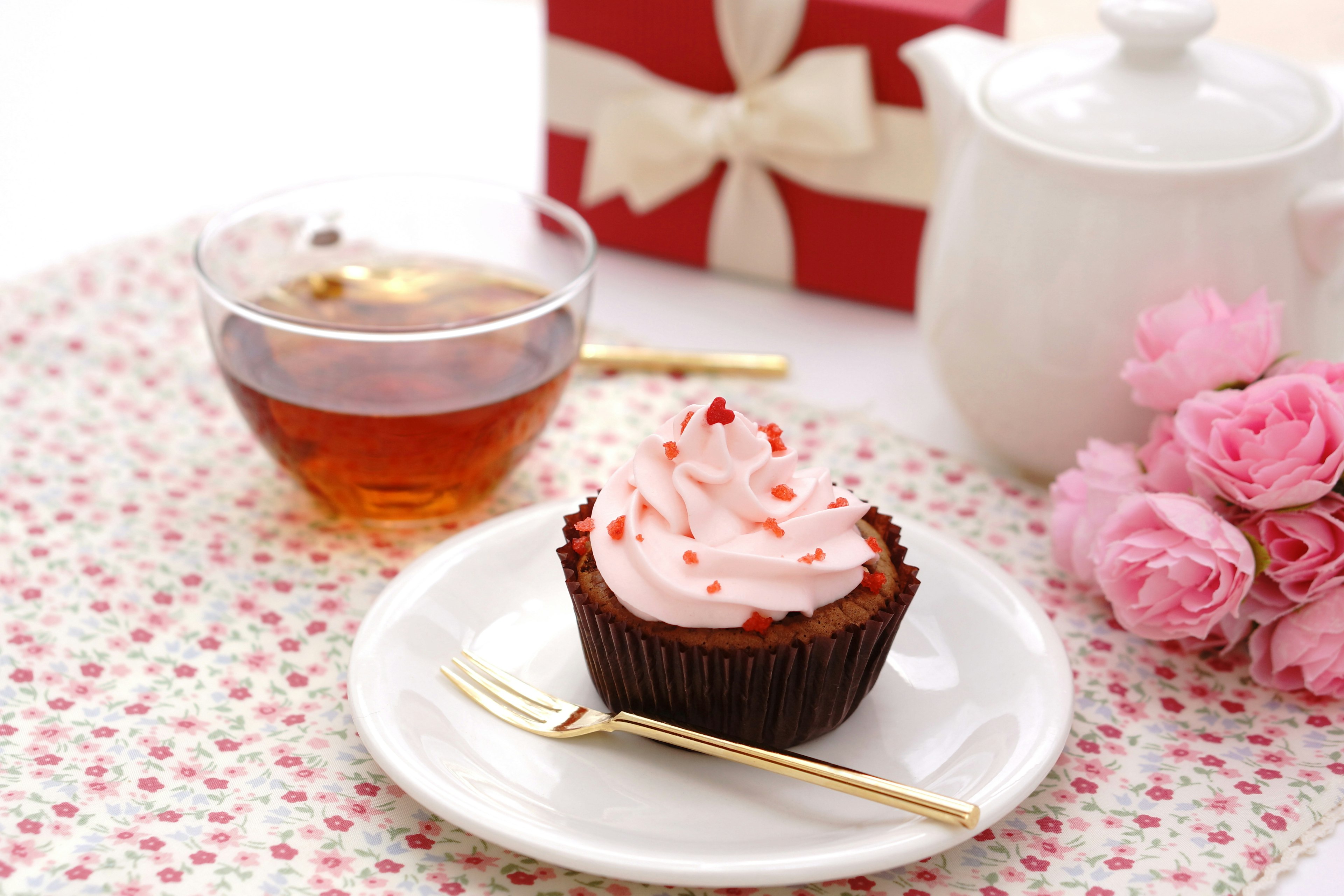 Un regalo con nastro rosso, tè, un cupcake con glassa rosa e rose rosa