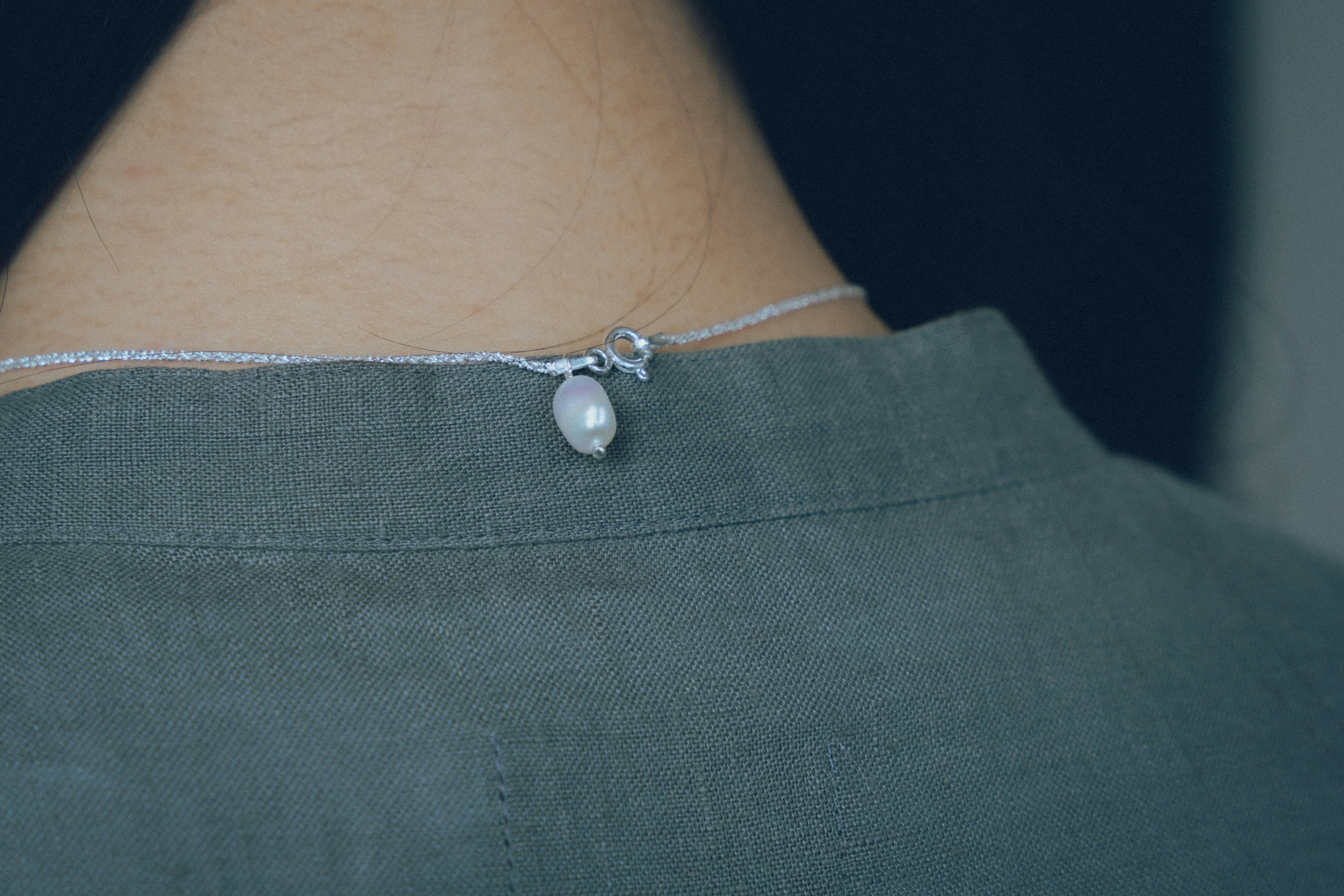 Chemise grise avec un collier de perles visible à l'arrière