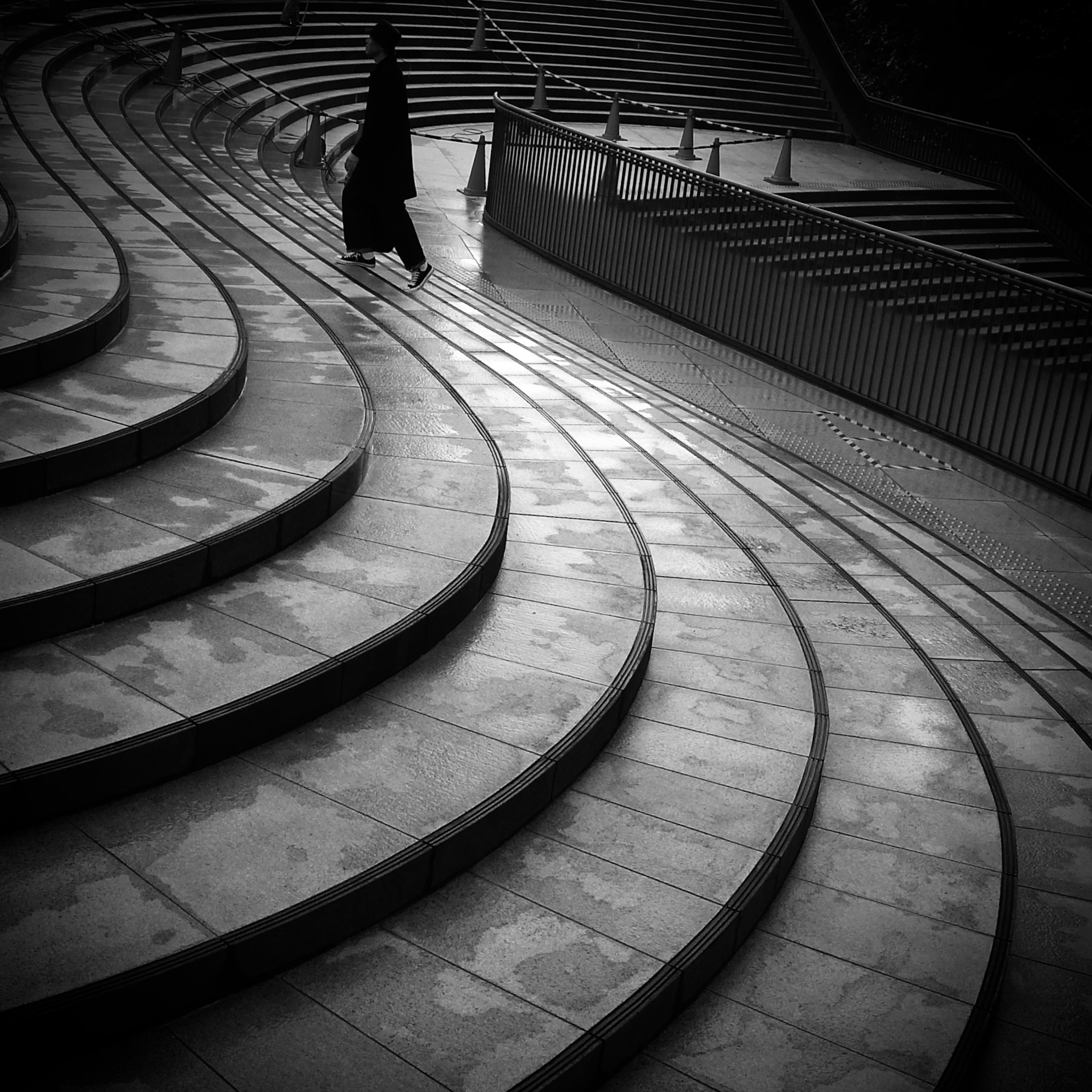 A person in a black coat walking down curved steps in a monochrome image