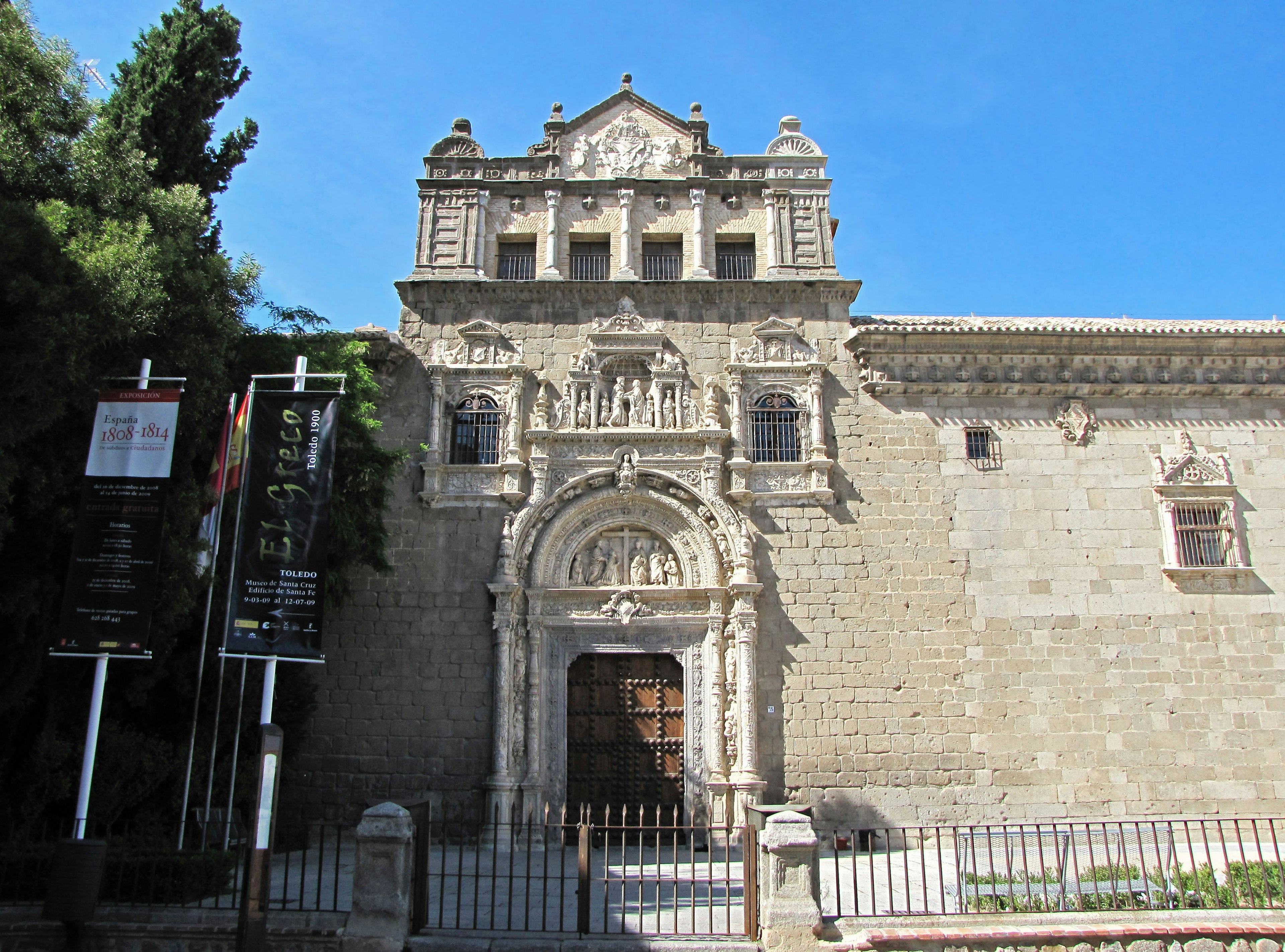 Historic building facade with decorative elements under a blue sky surrounded by green trees