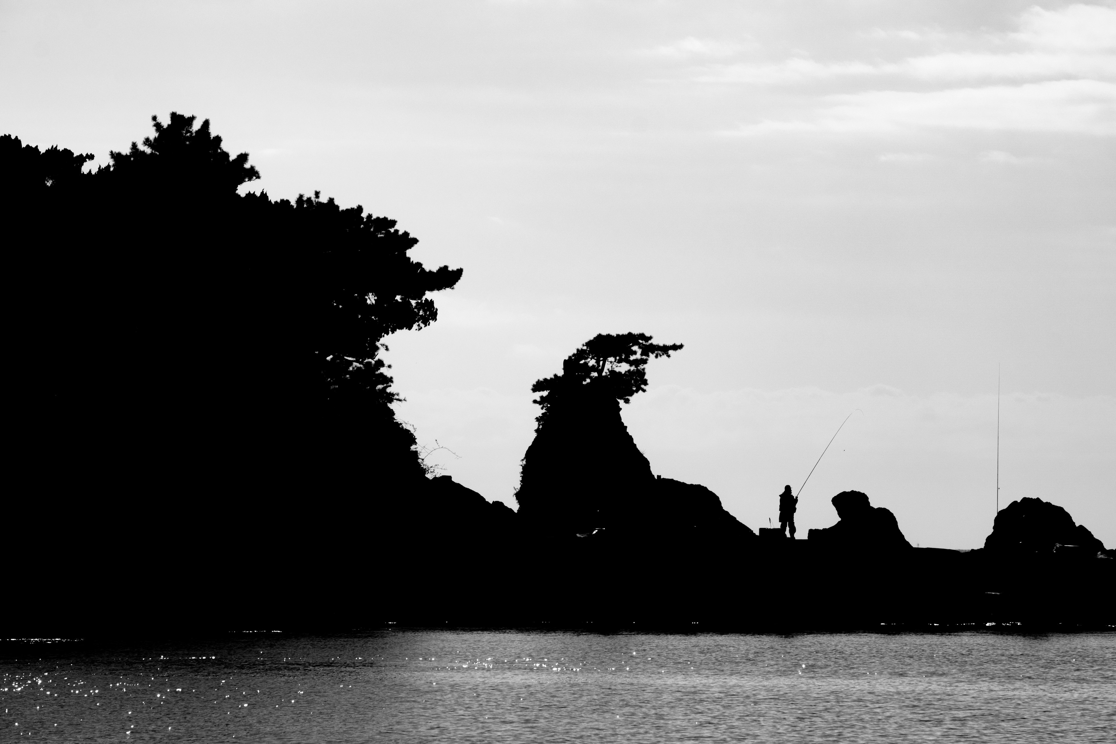 Silhouette von Bäumen und Felsen mit einer Person im Hintergrund