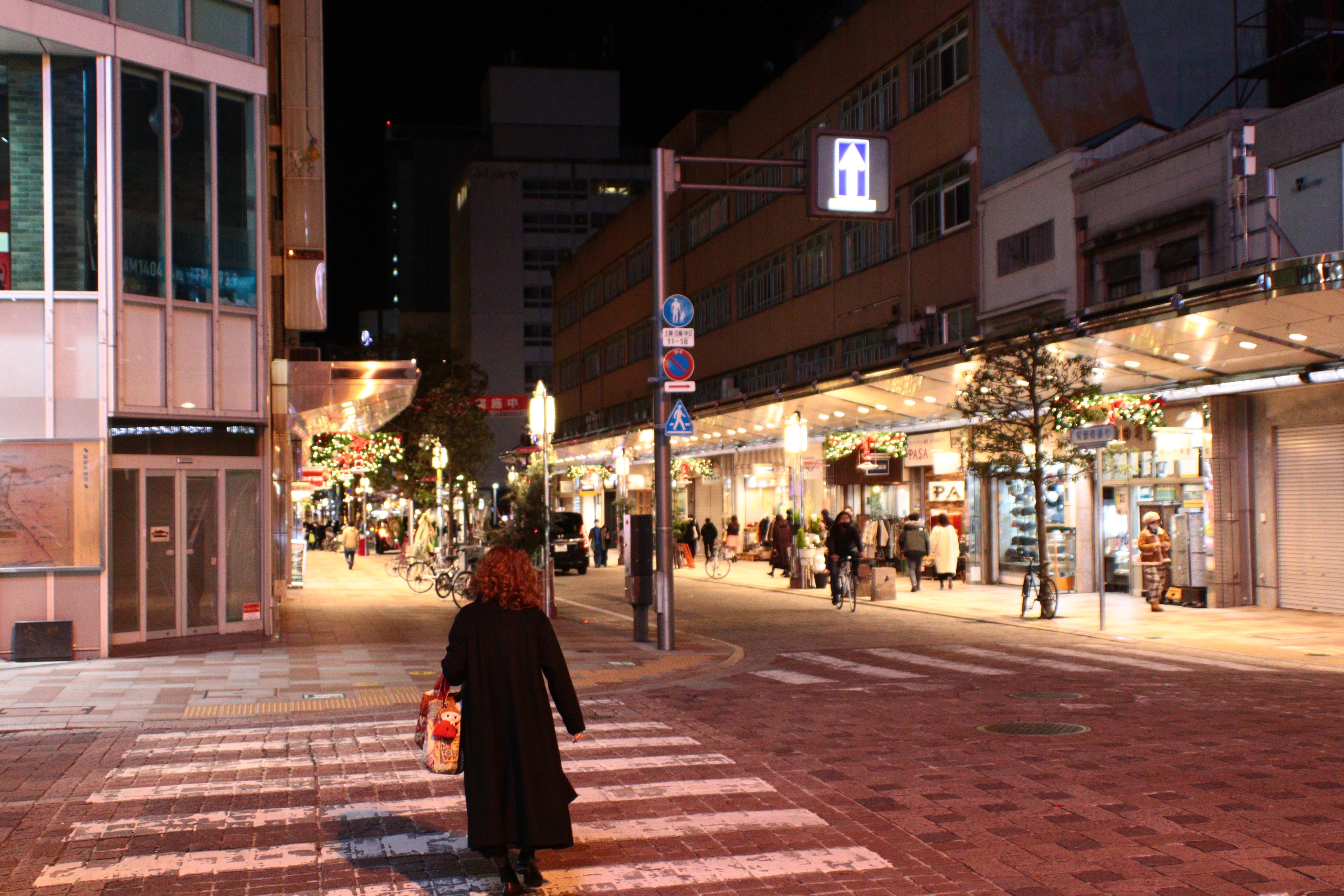 Mujer caminando en una calle de la ciudad por la noche con tiendas iluminadas