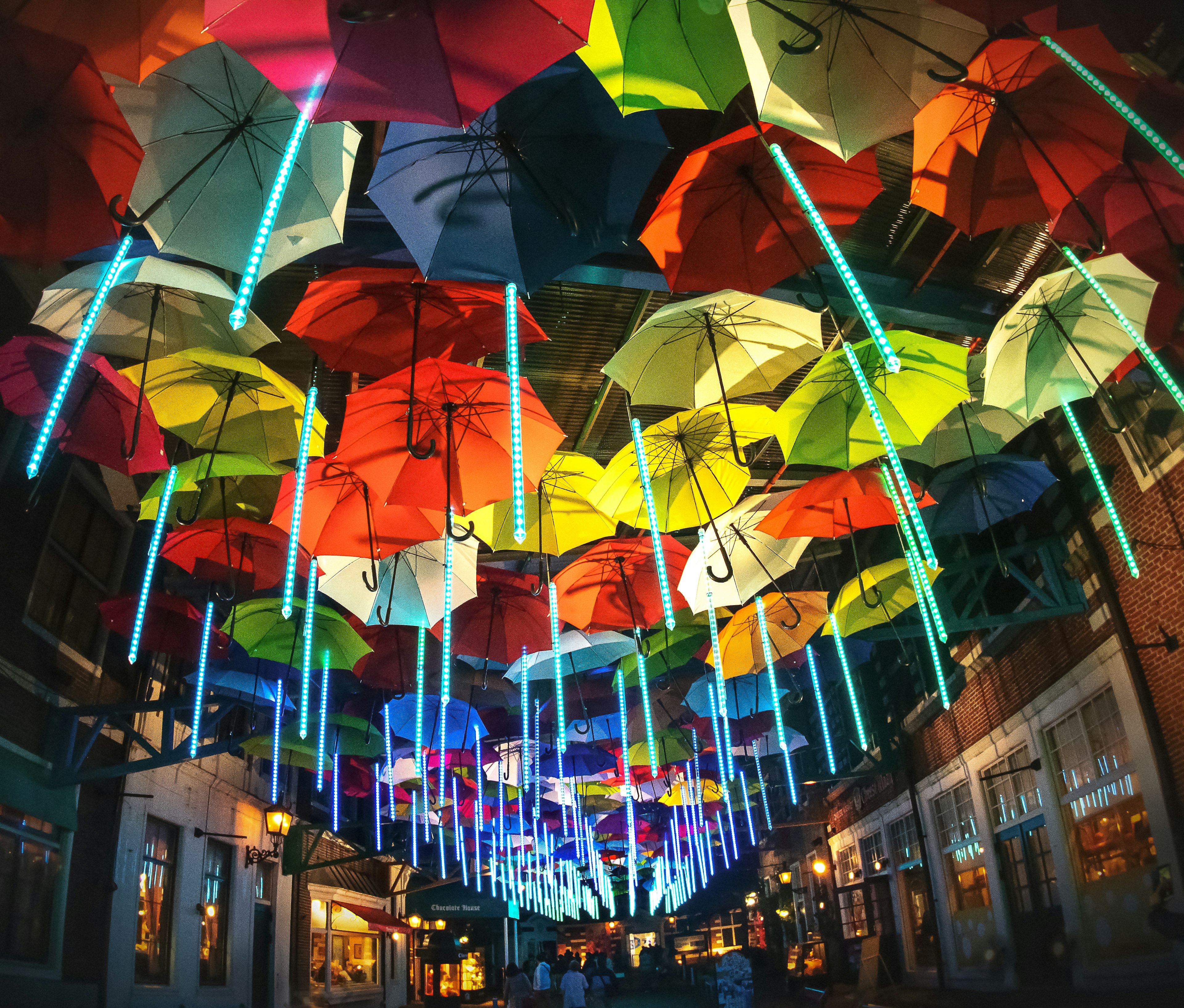 Una escena vibrante de la calle con paraguas coloridos colgando y iluminados por luces de neón brillantes