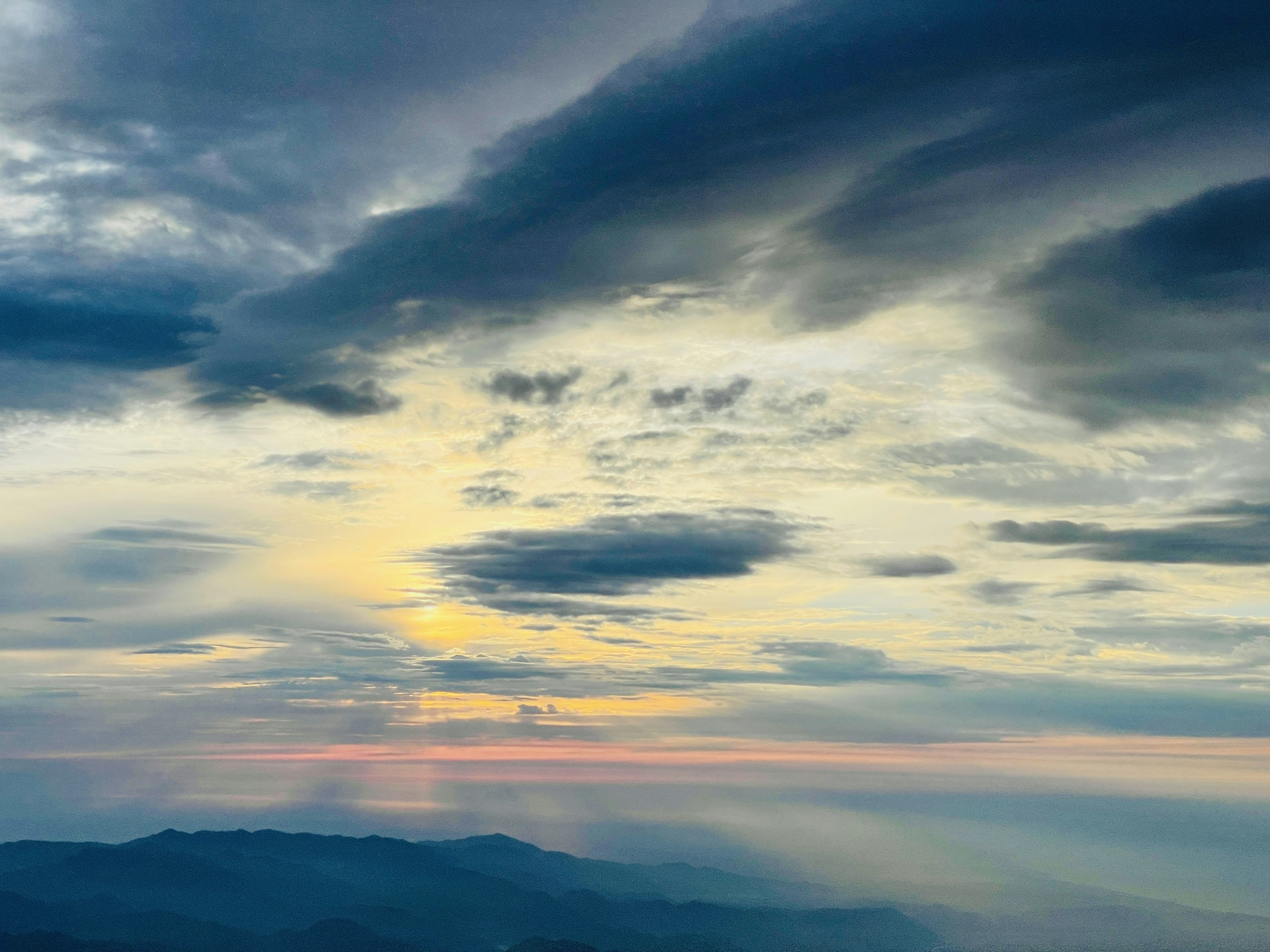 Vista mozzafiato del tramonto dalla cima di una montagna con nuvole e un gradiente da arancione a blu