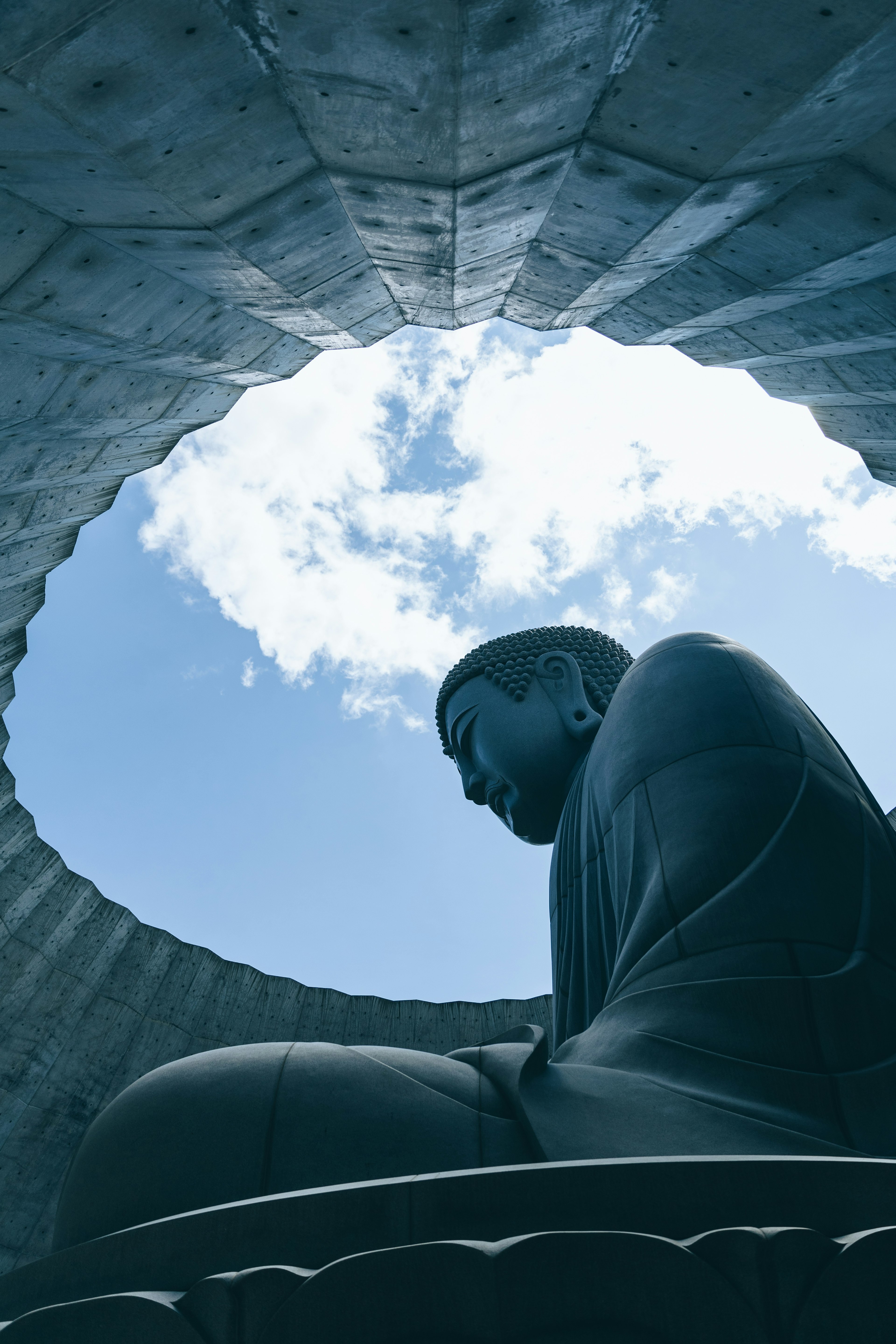 Silhouette einer Buddha-Statue vor einem hellblauen Himmel, eingerahmt von einer kreisförmigen Struktur