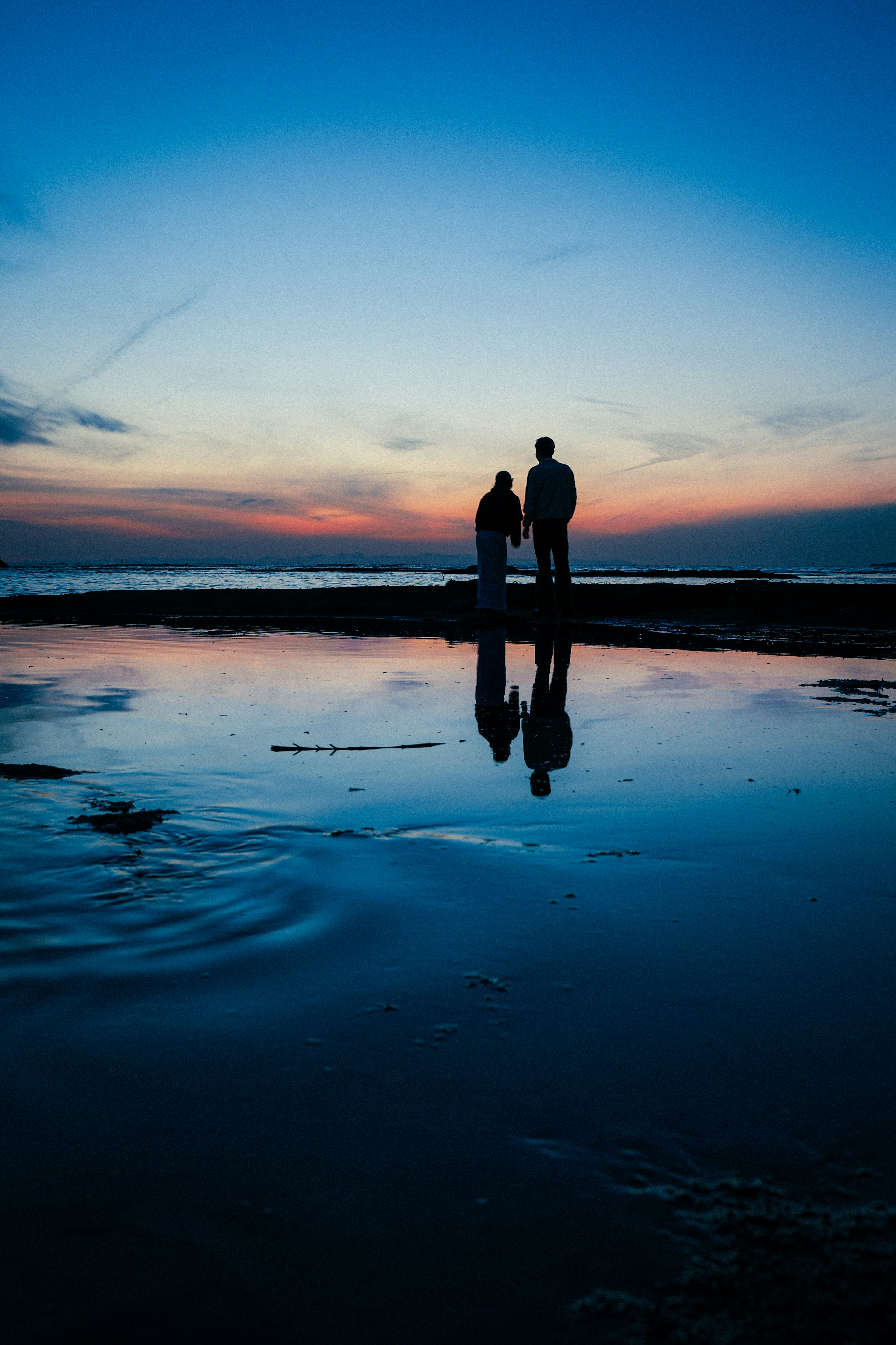 Silhouette di due persone in piedi sulla riva al tramonto con riflessi sull'acqua