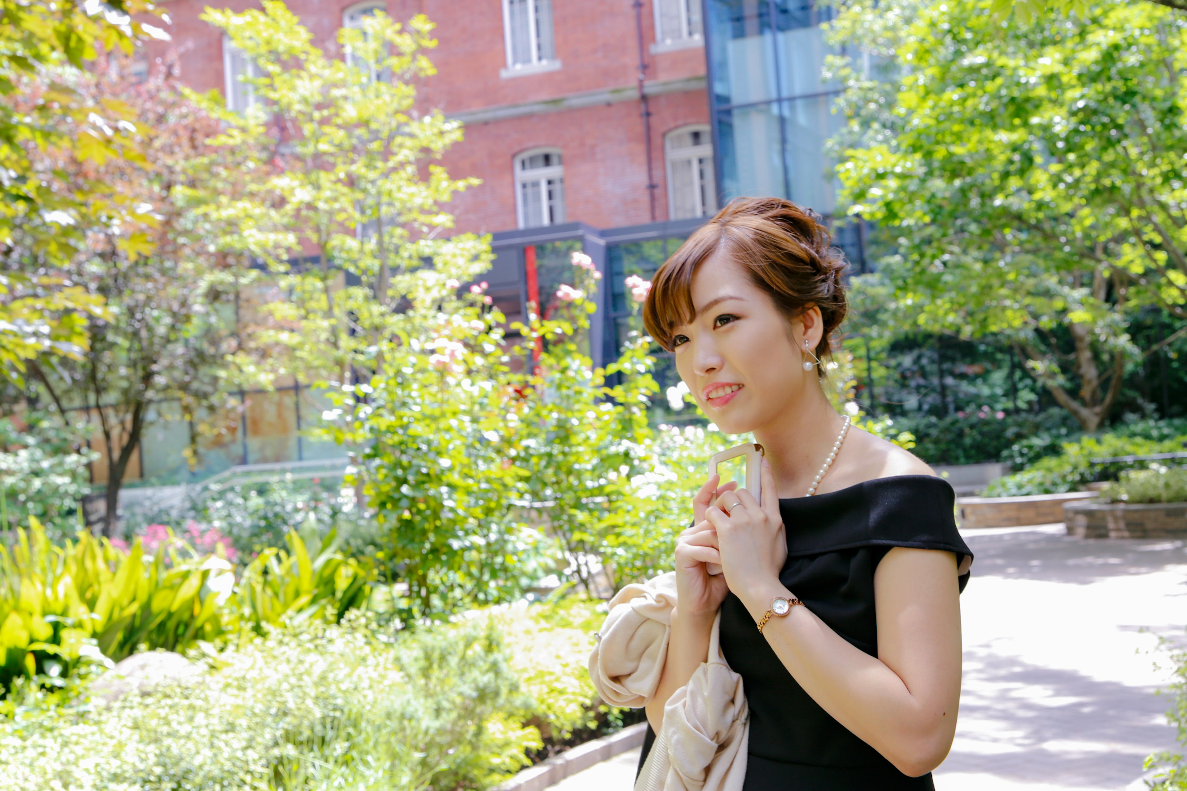 A woman in a black dress smiling in a park surrounded by greenery