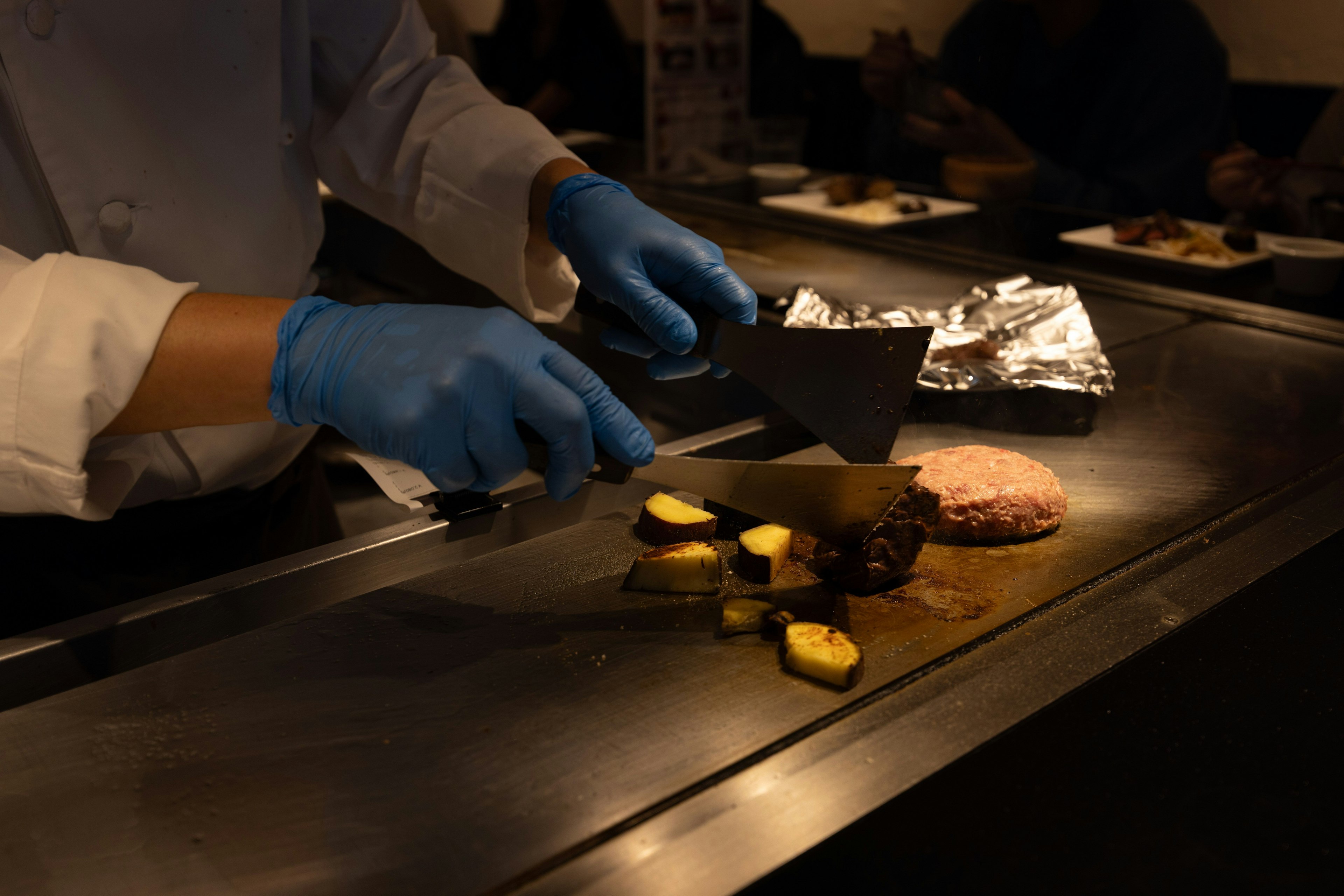Koch mit blauen Handschuhen, der Essen auf einem Teppanyaki-Grill zubereitet