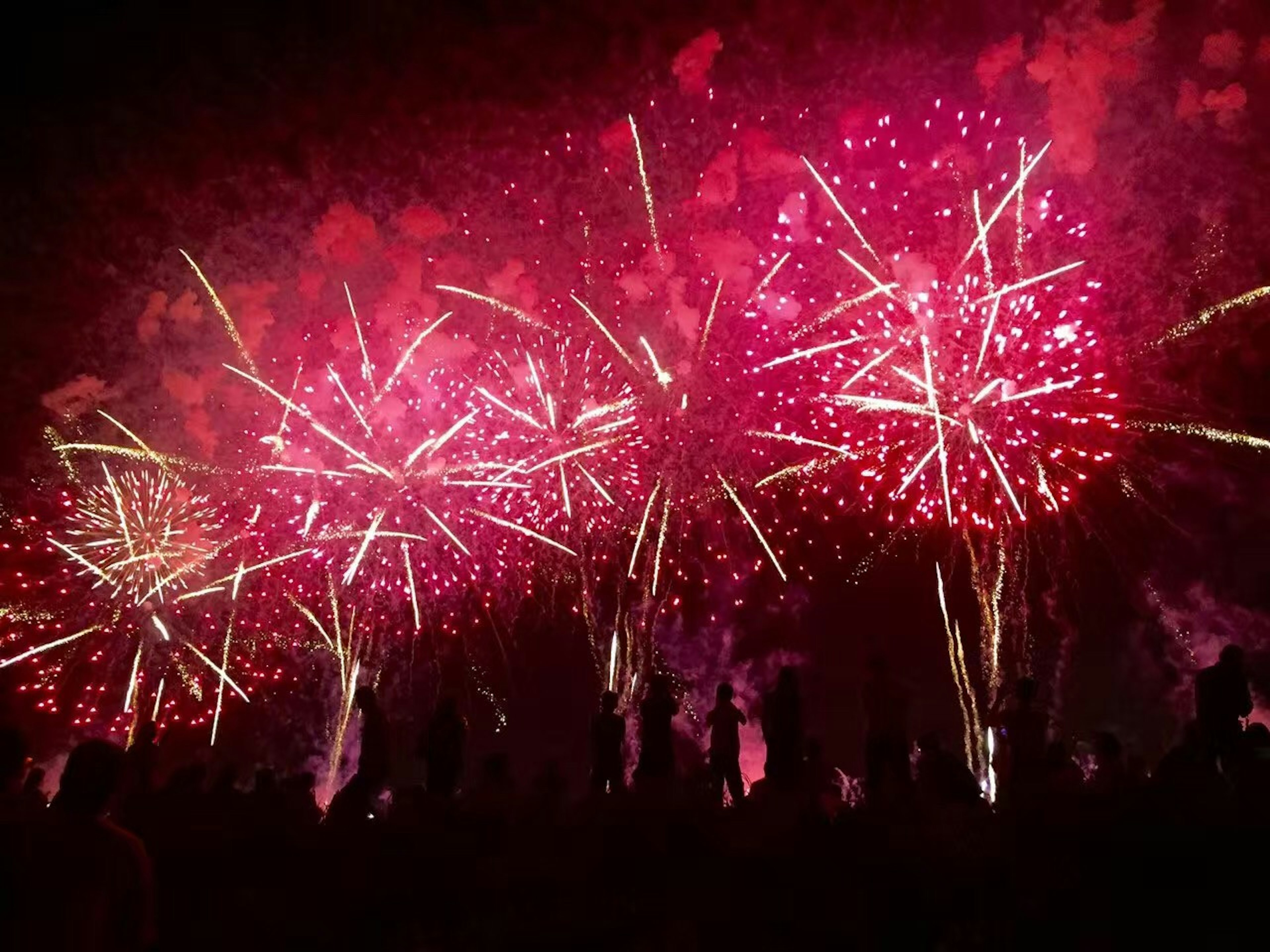 A display of red fireworks lighting up the night sky with silhouettes of spectators