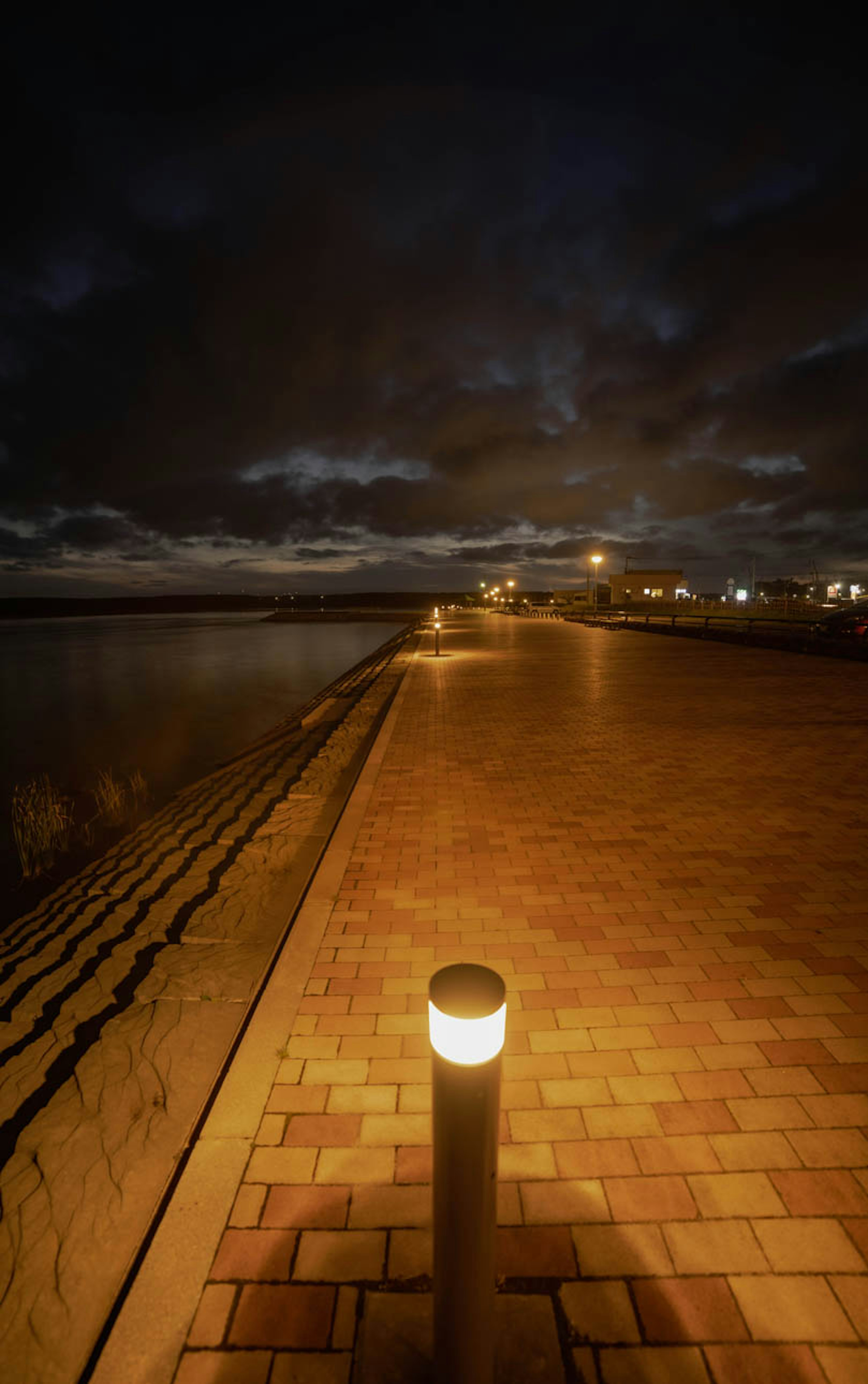 Pflasterweg entlang der Küste bei Nacht mit beleuchtetem Pfosten und bewölktem Himmel