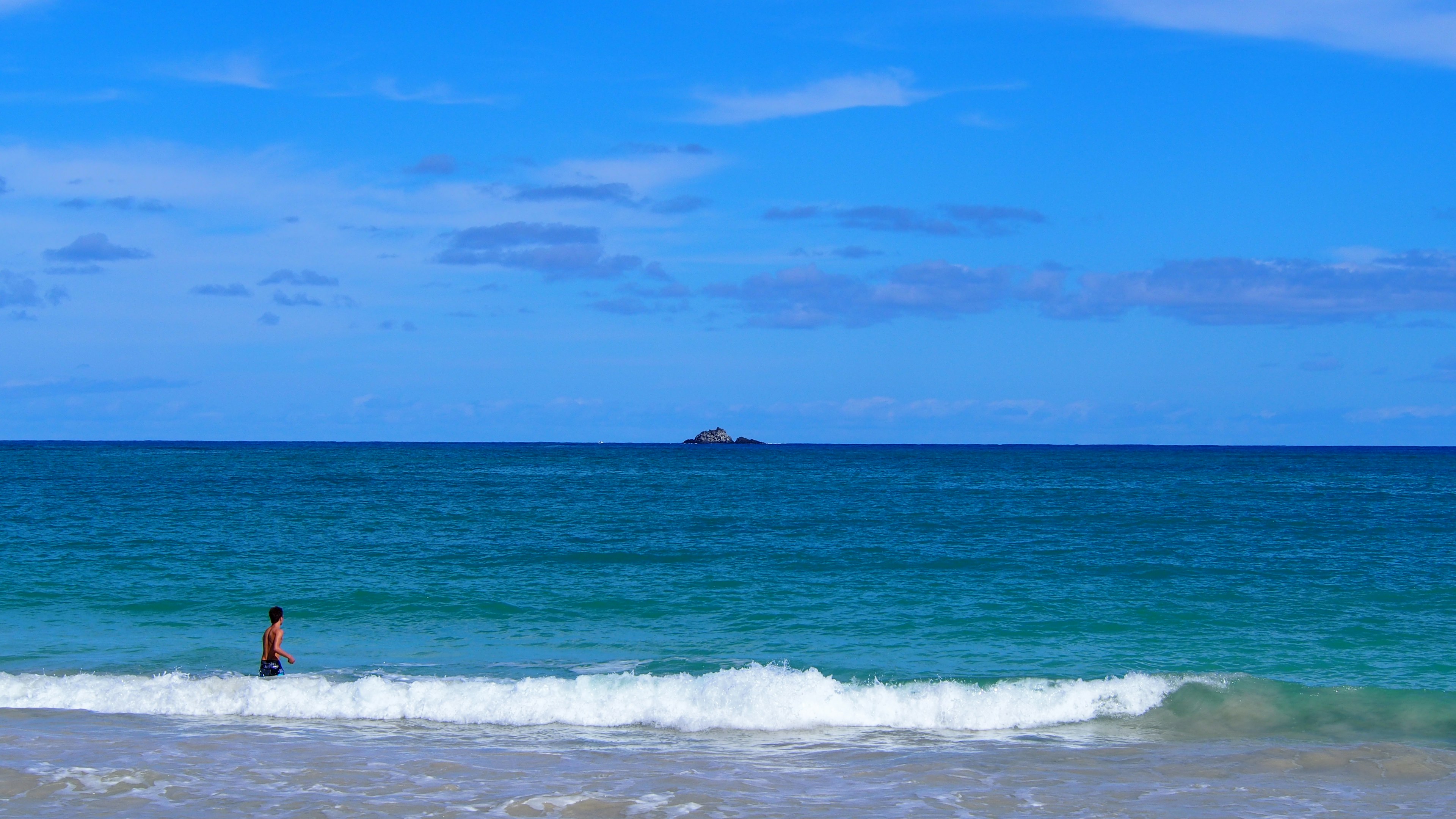 Person wading in the ocean under a blue sky