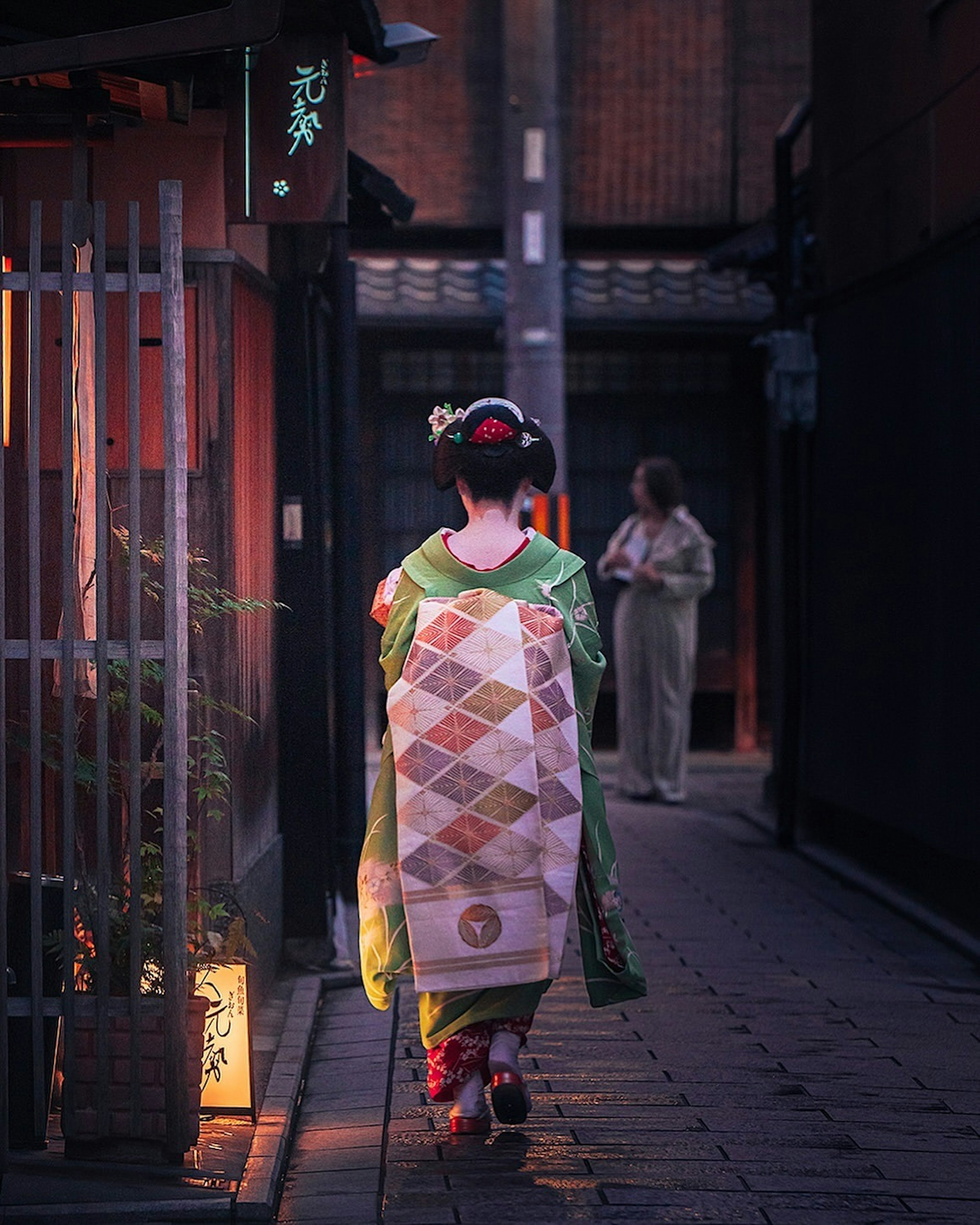 Una donna in kimono che cammina di sera con un'altra persona sullo sfondo