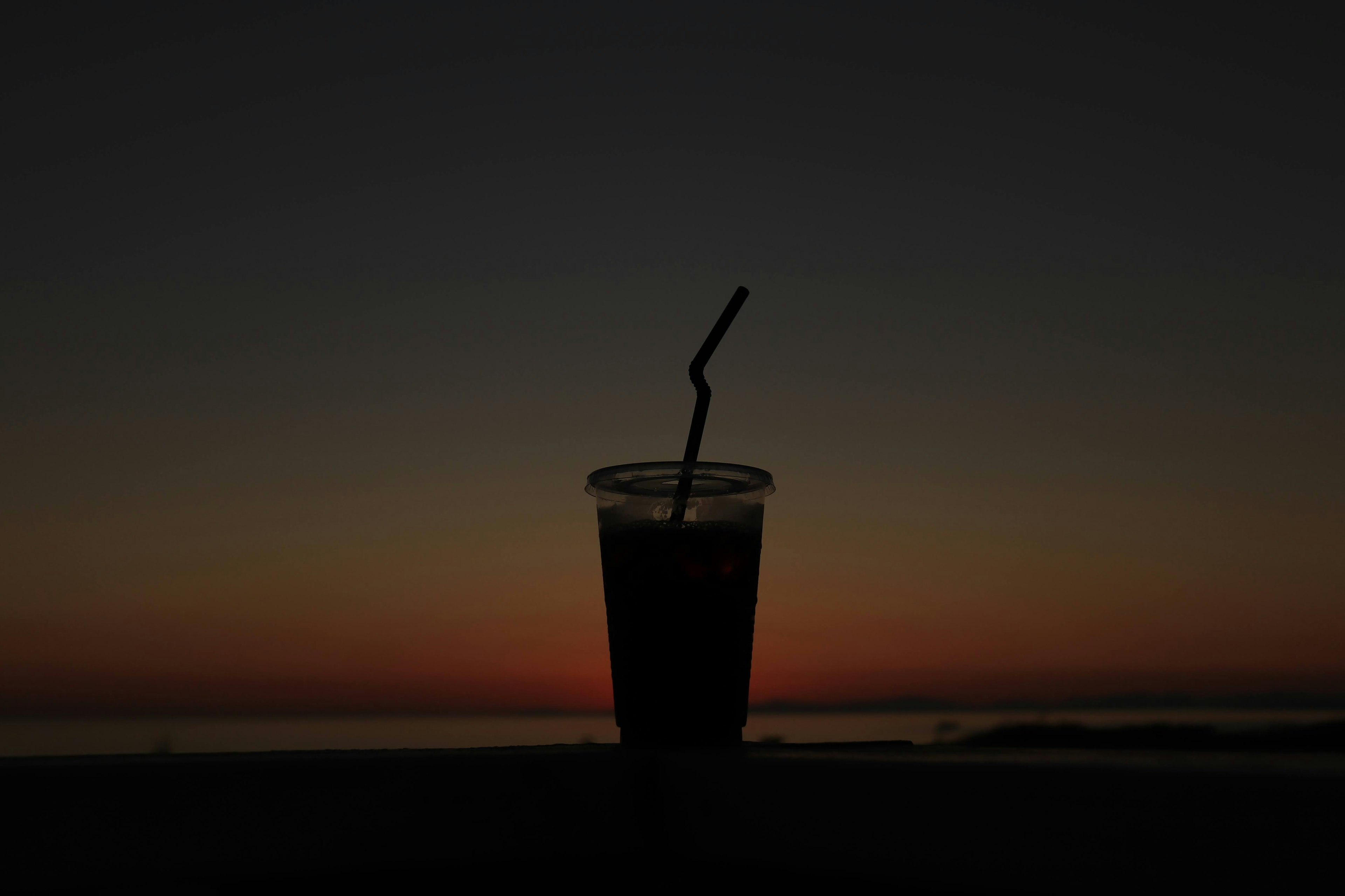 Silhouette de un vaso de bebida con una pajilla contra un fondo de atardecer