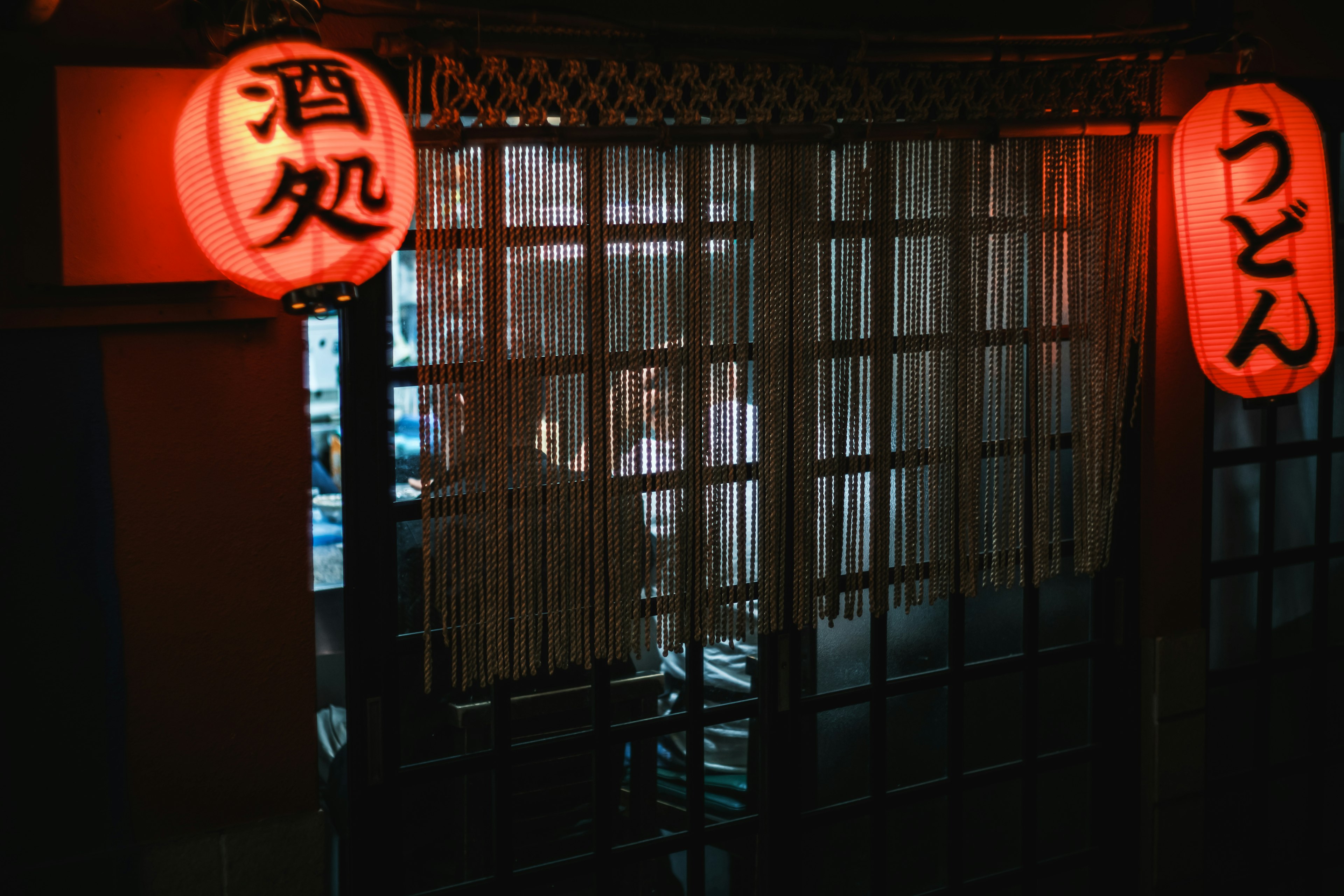 Außenansicht eines japanischen Izakaya mit roten Laternen und der Silhouette einer Person