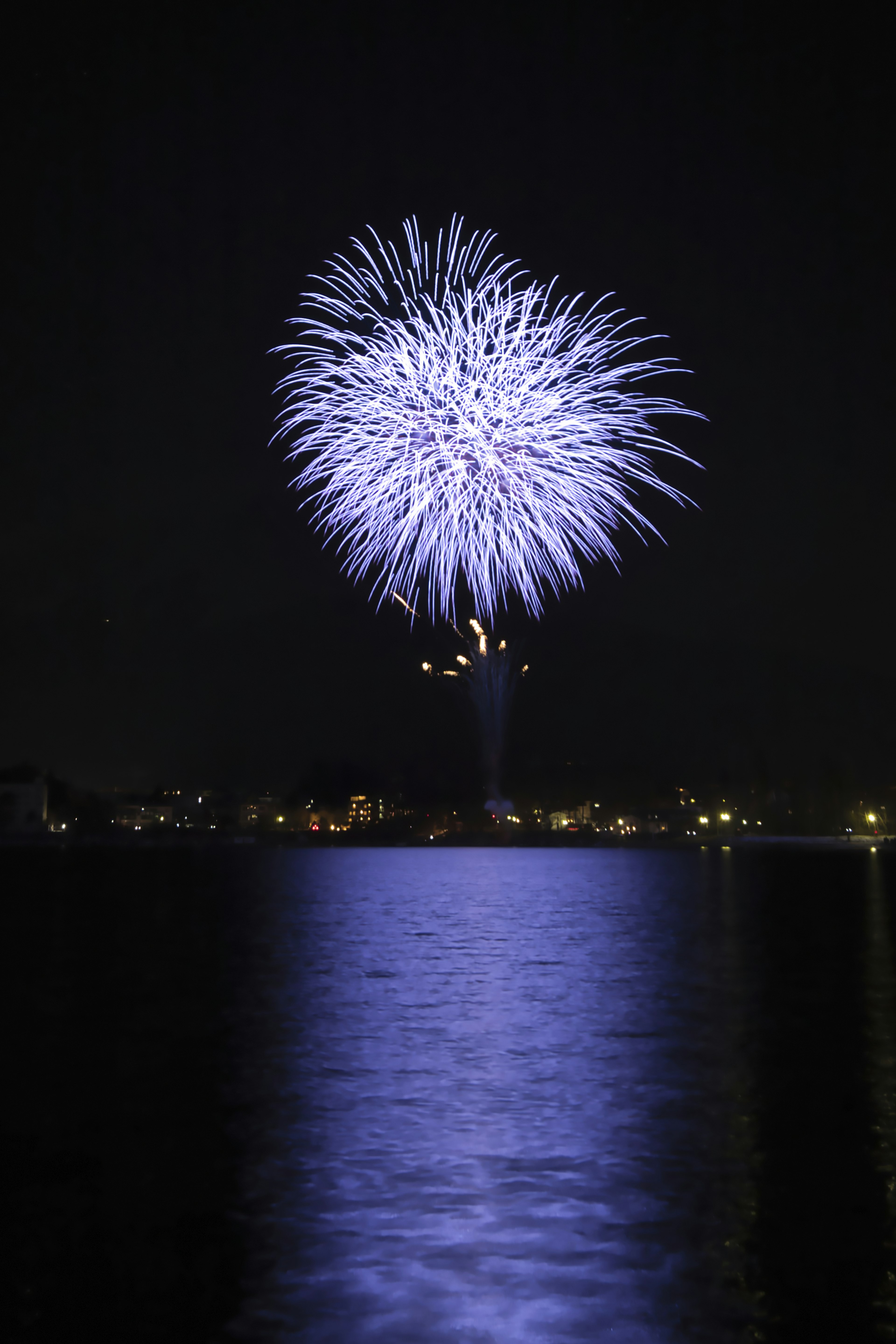 Wunderschöne Szene von lila Feuerwerk, das am Nachthimmel blüht und sich im Wasser spiegelt