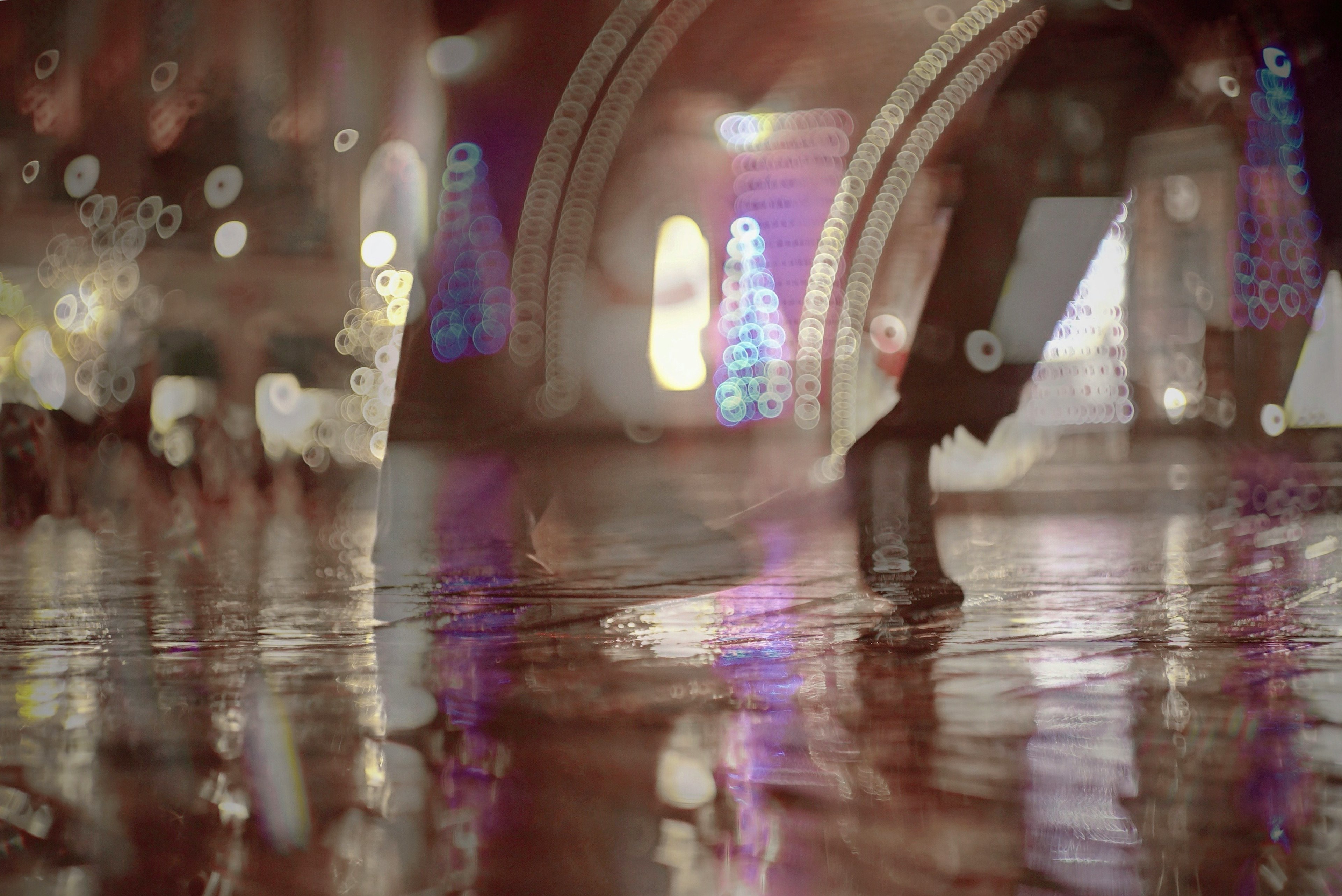 Feet walking on a wet surface reflecting colorful city lights