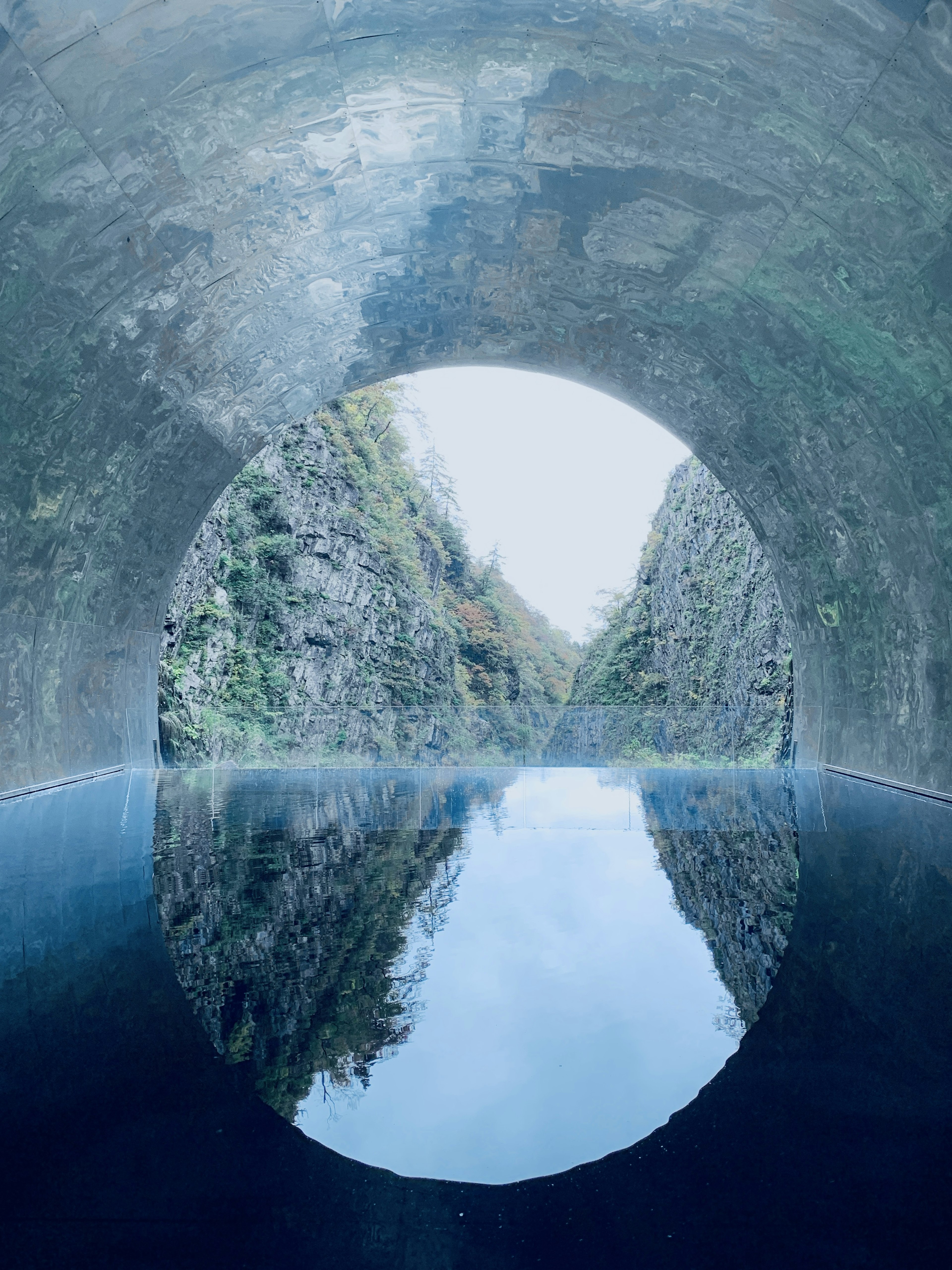 Vista desde el interior de un túnel que muestra un reflejo circular en el agua tranquila rodeado de paredes rocosas