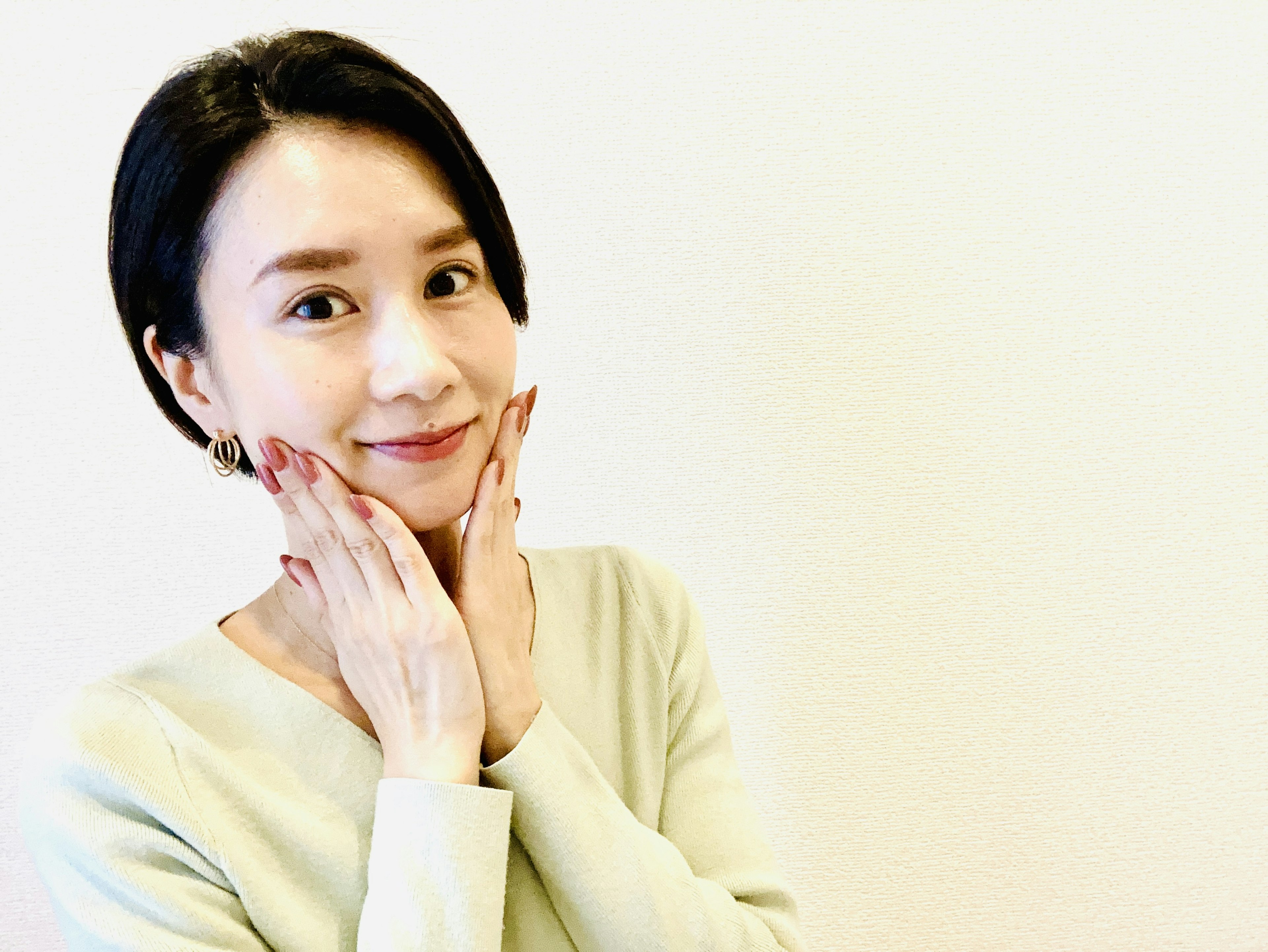 A woman smiling with her hands on her face against a simple background