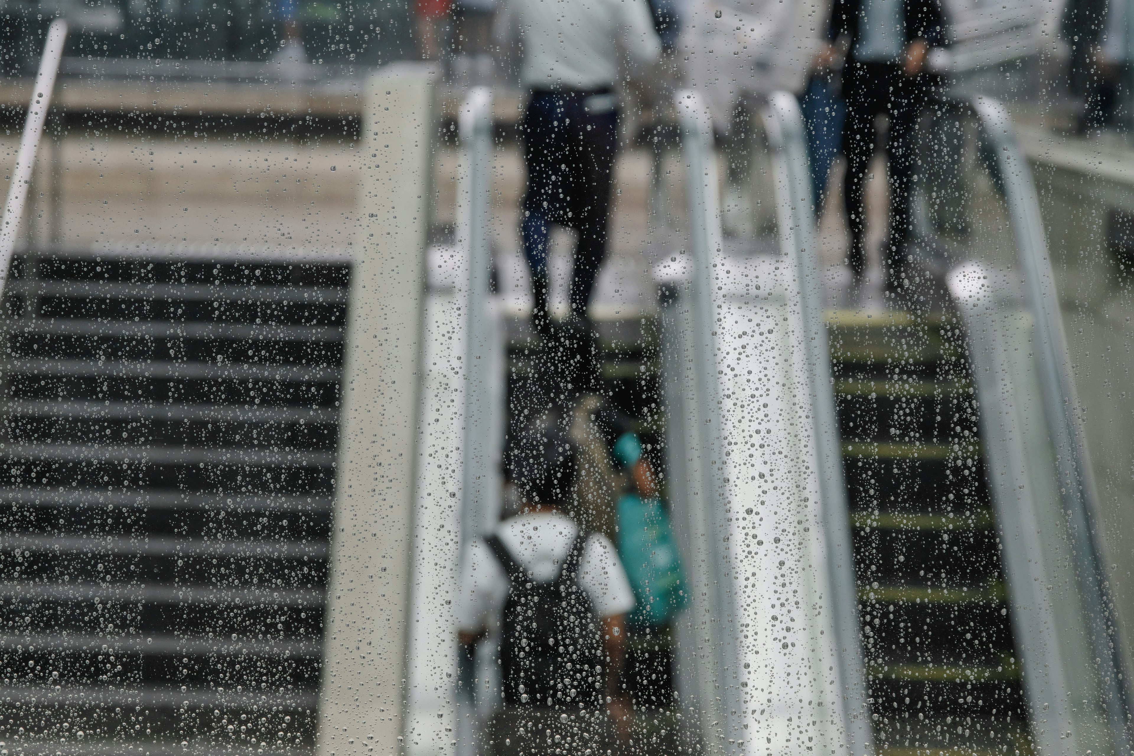 Personnes descendant des escaliers vues à travers une vitre avec des gouttes de pluie