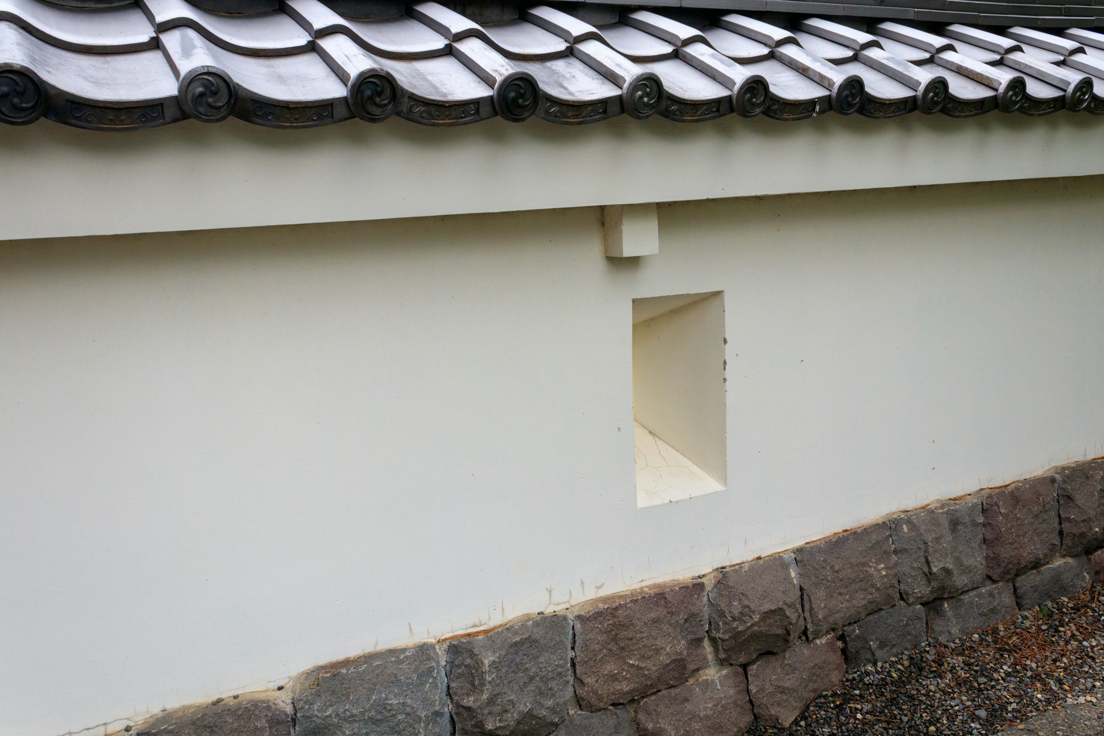 Side view of a traditional building with a white wall and stone foundation featuring a window-like opening