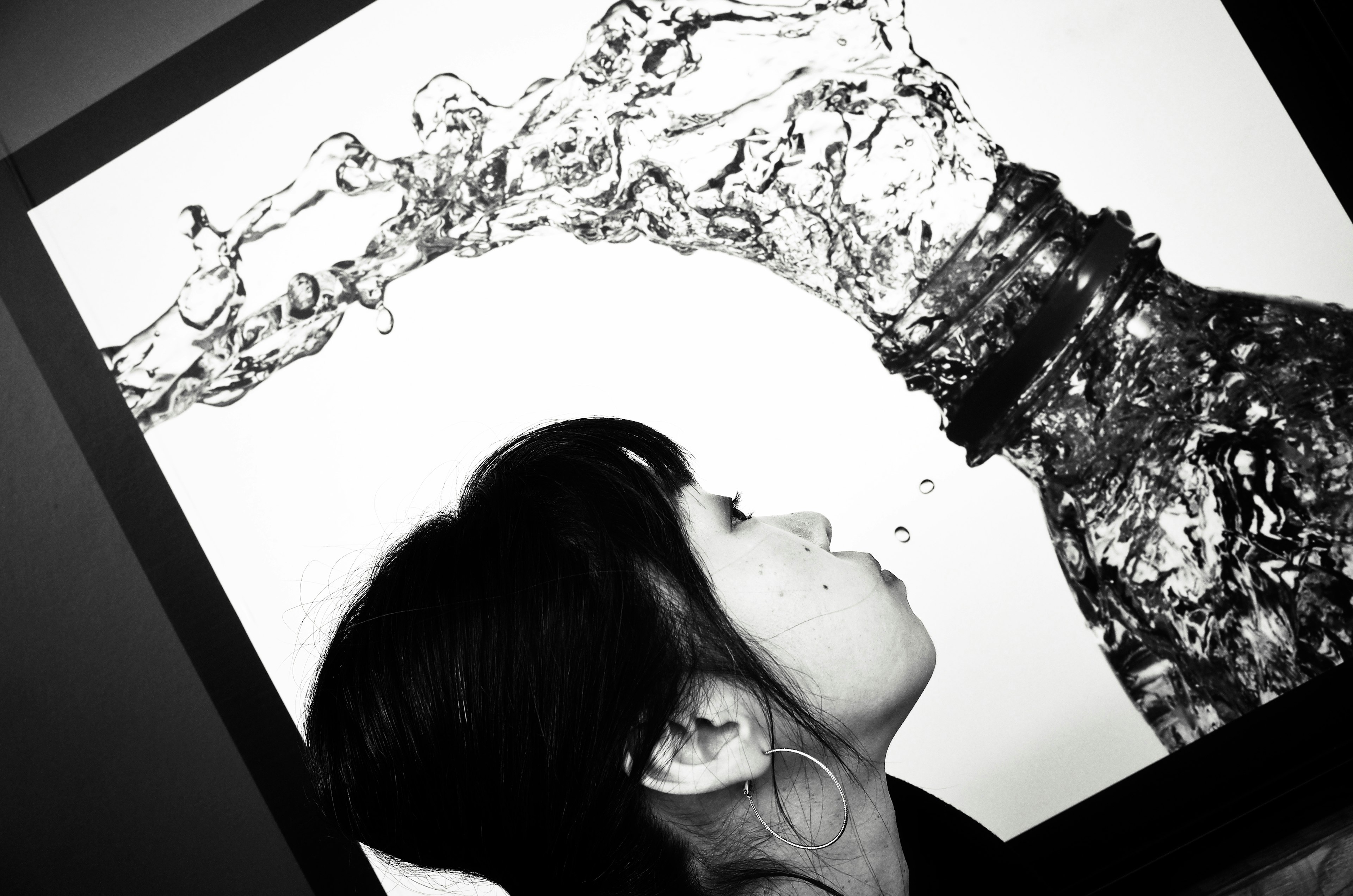 Black and white photo of a woman drinking water with flowing liquid from a bottle