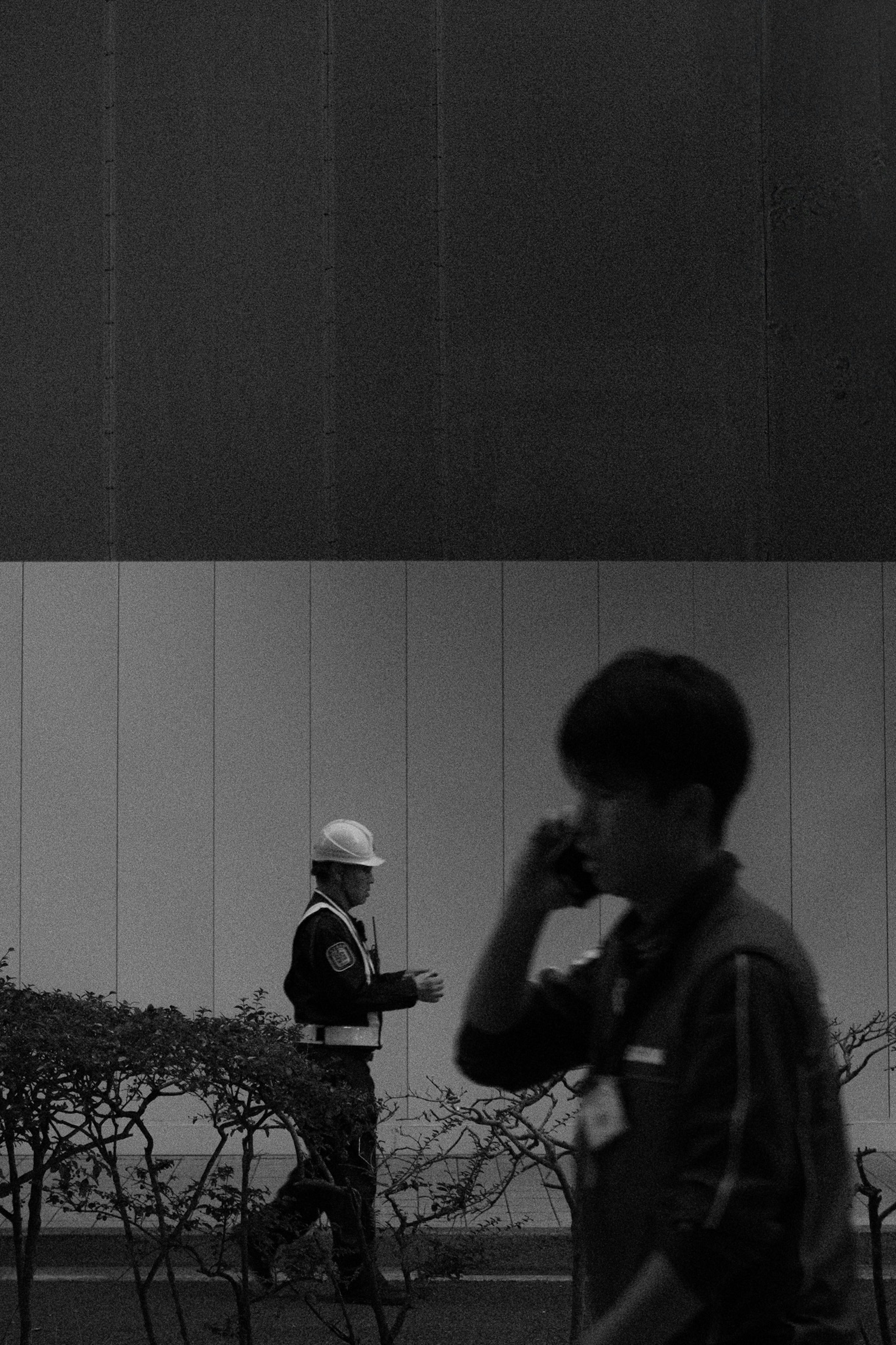 Construction worker in a helmet walking while a young man is talking on the phone