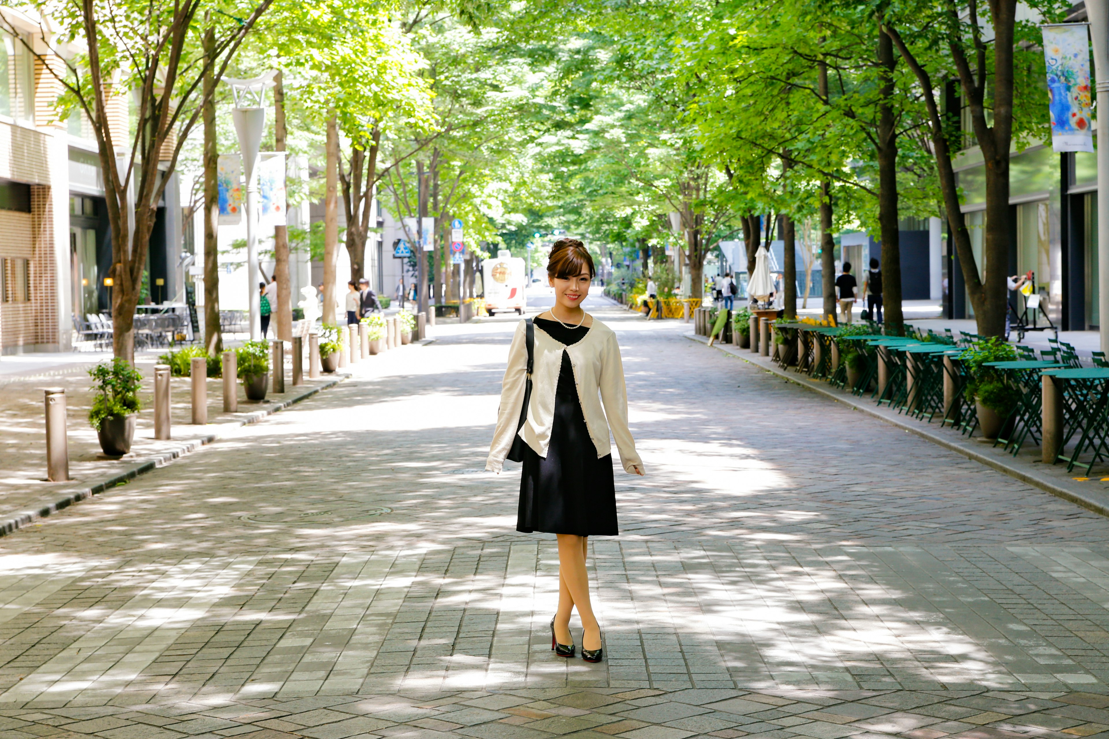 A woman in a black dress standing on a tree-lined street