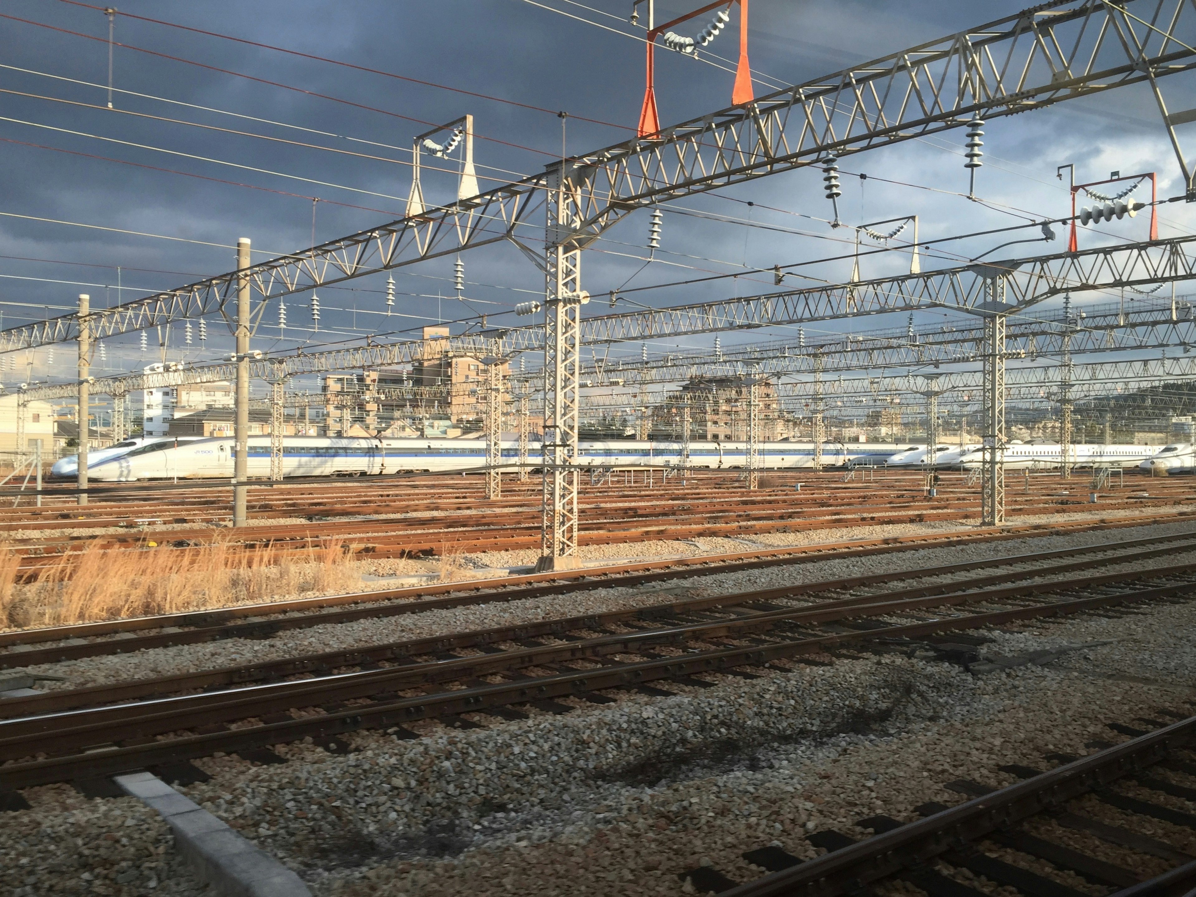 View of railway overhead lines and tracks under a cloudy sky with urban background