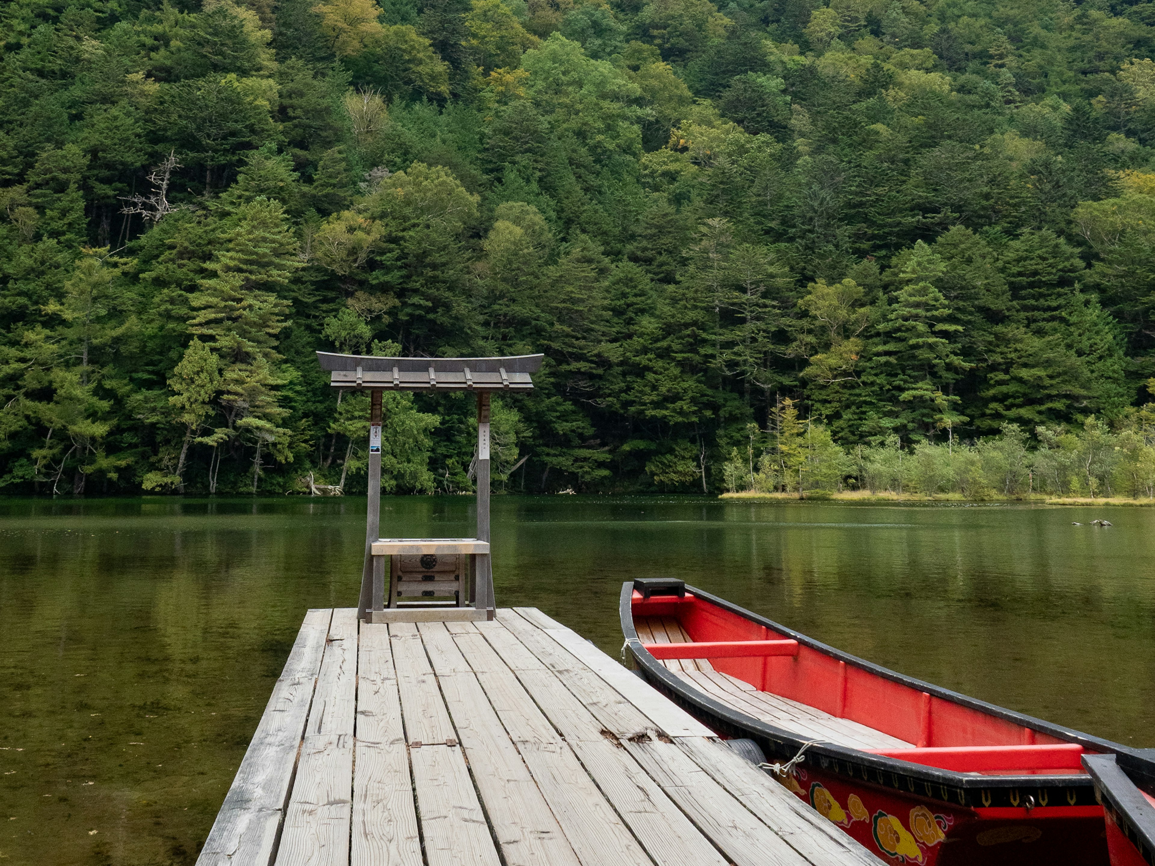 Serene lakeside dock surrounded by green trees and a red boat