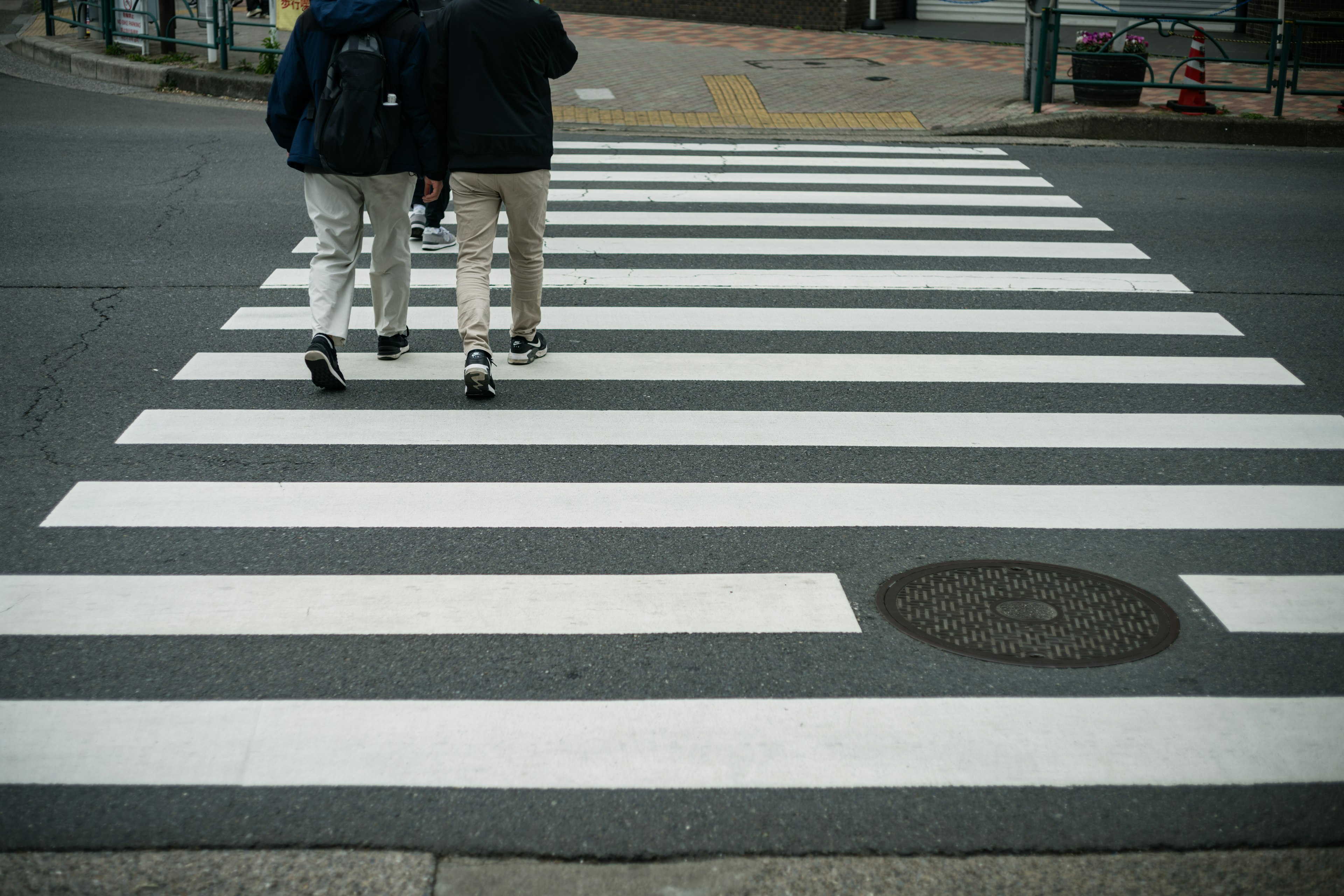 Zwei Personen gehen auf einem schwarz-weißen Zebrastreifen